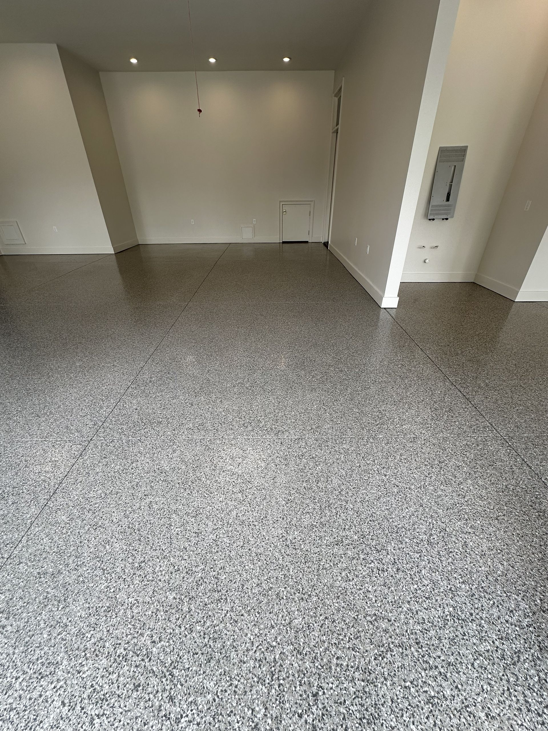 Empty room with speckled gray flooring, white walls, and an electrical panel.