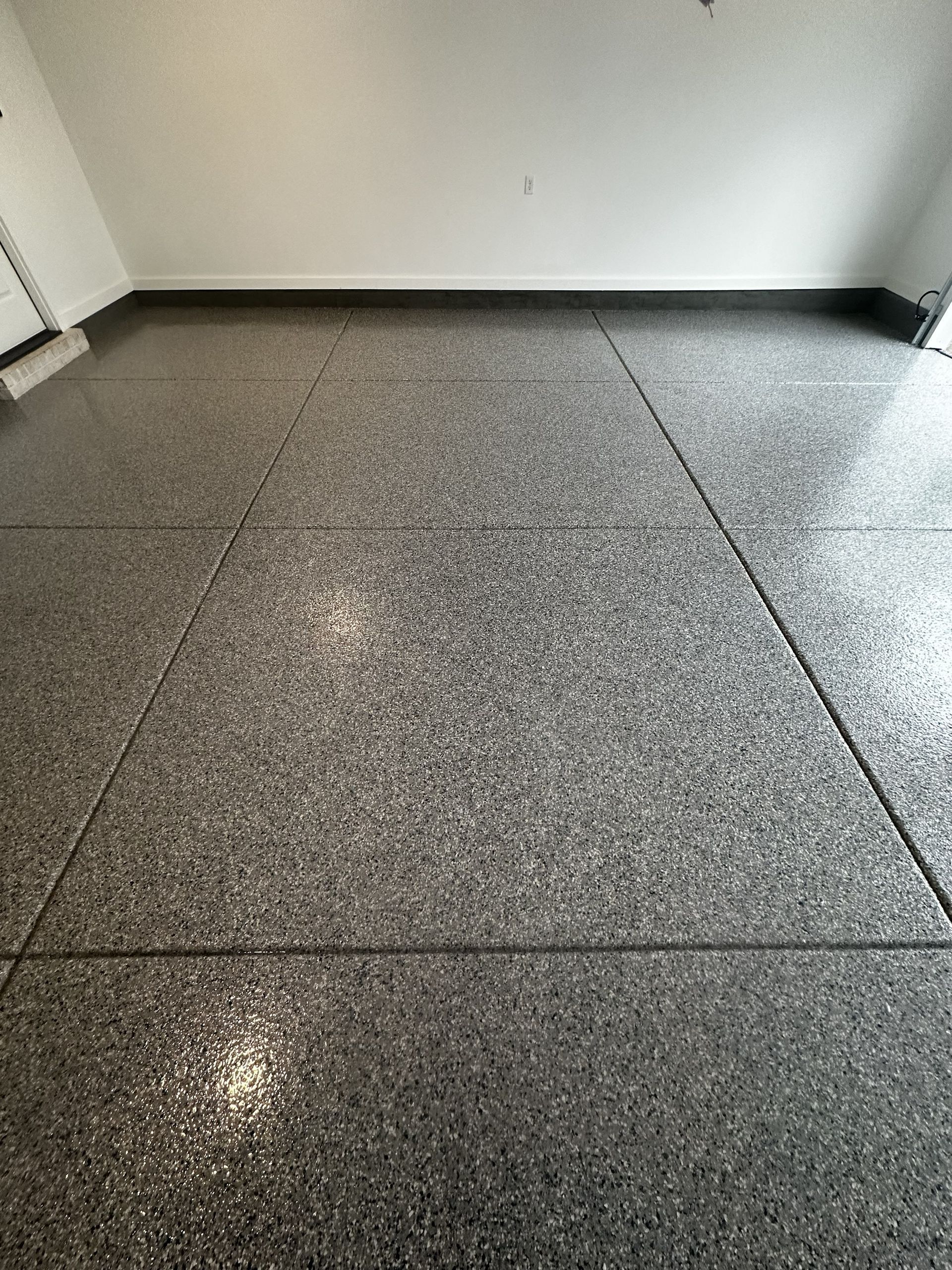 Garage floor with a speckled epoxy coating, gray and shiny, with visible expansion joints.