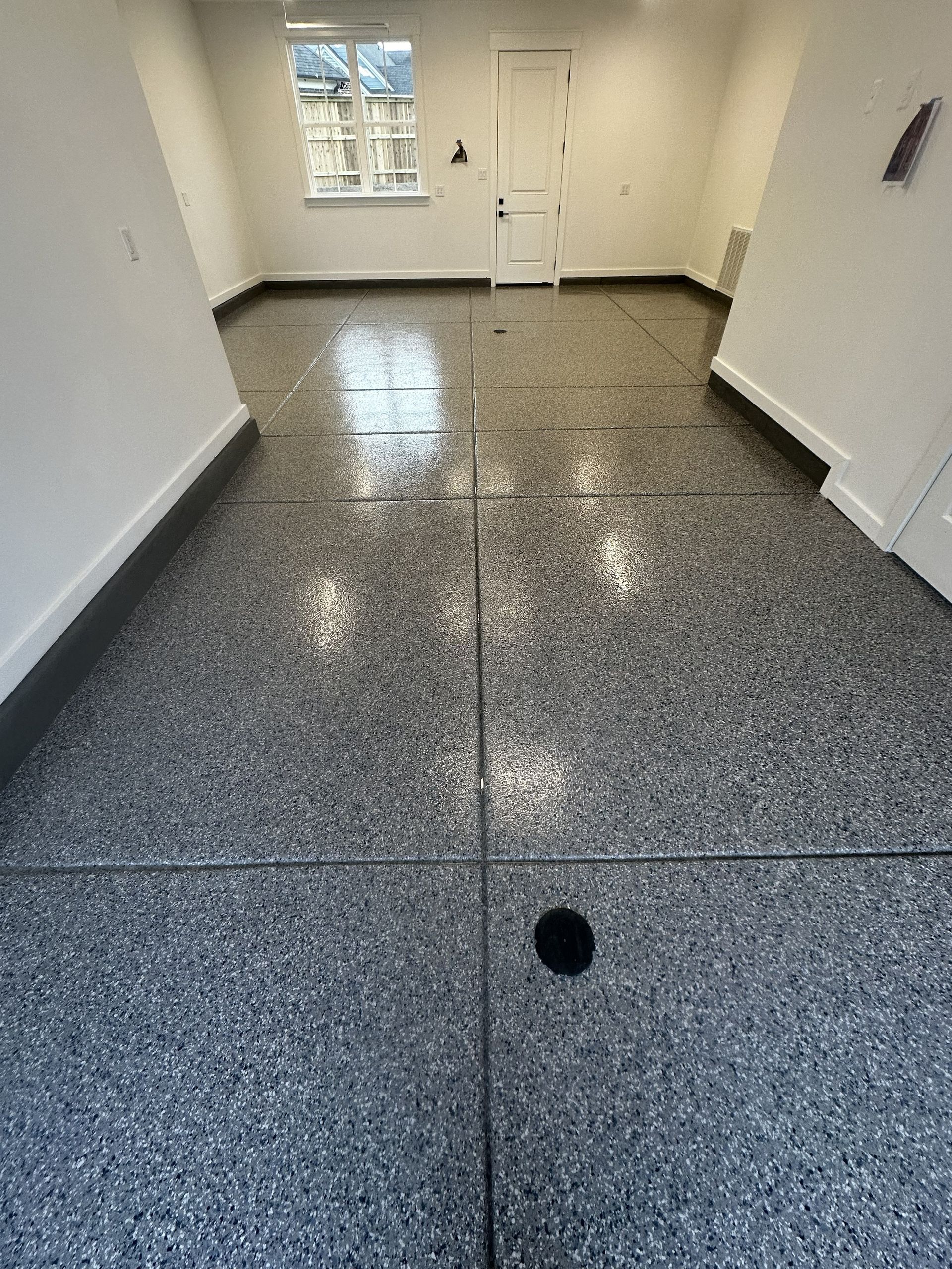 Gray epoxy floor in a room, with a drain and a window in the background.