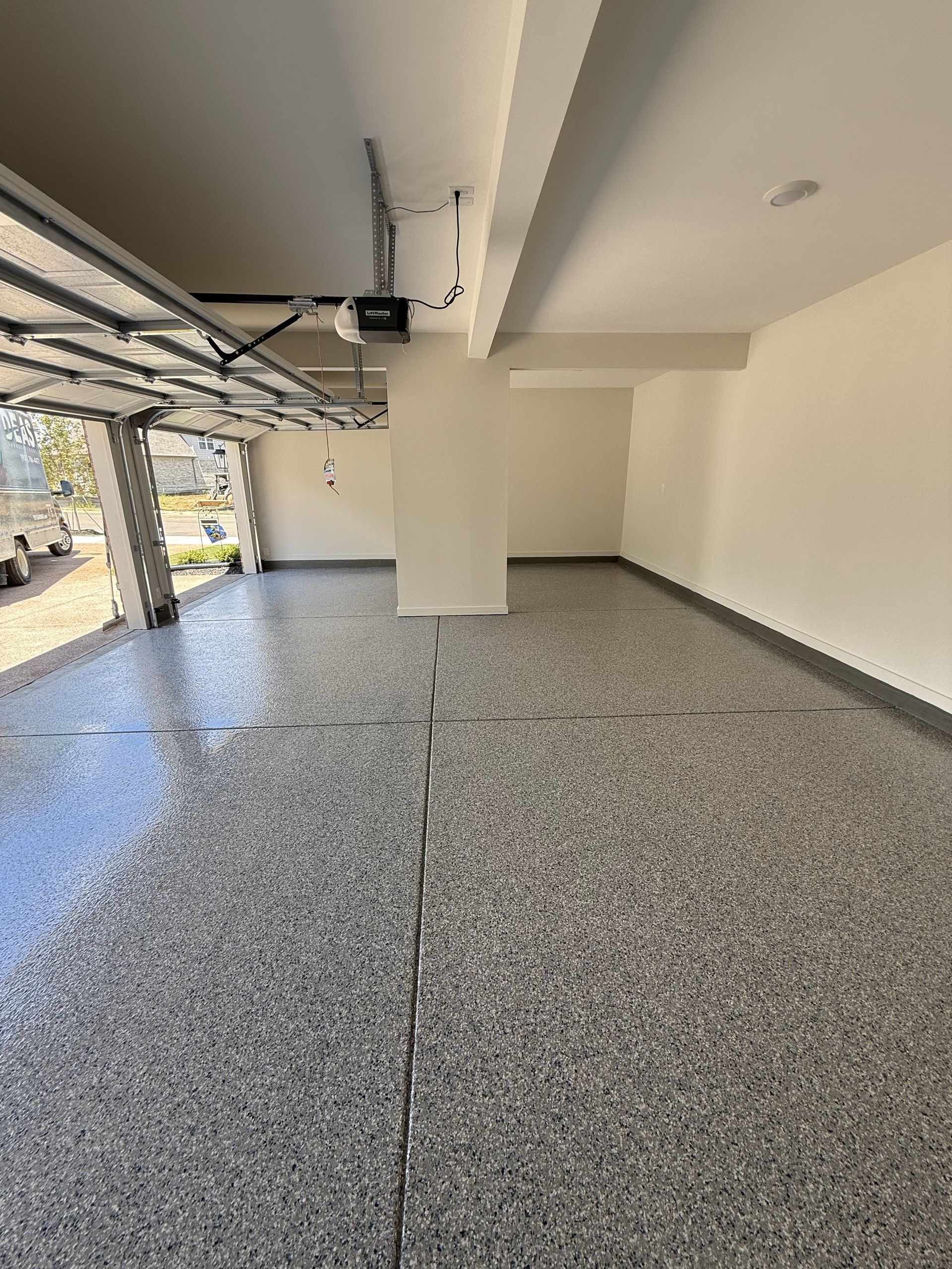 An empty garage with a garage door open and a gray floor.