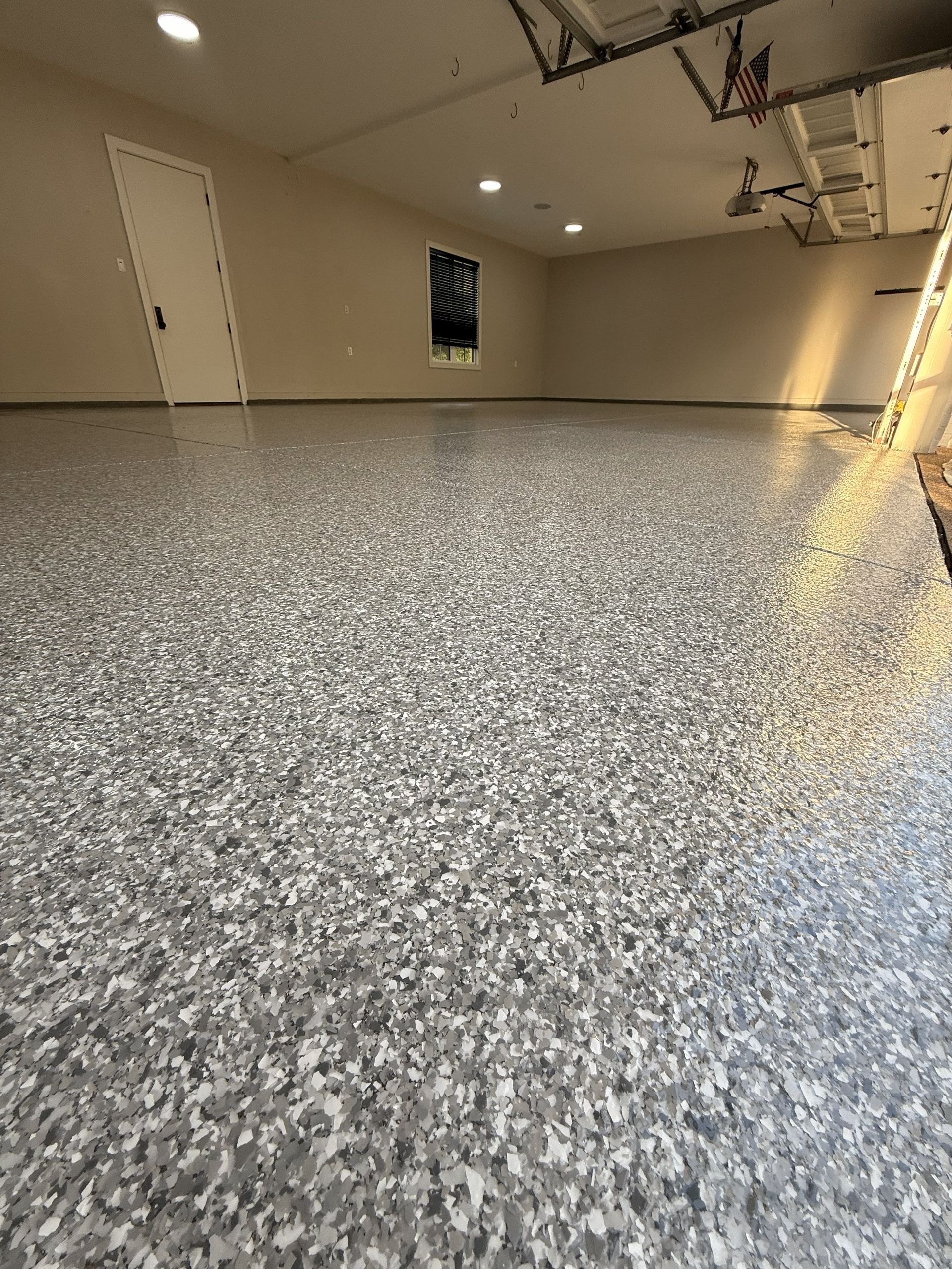 Garage interior with a speckled, light-colored epoxy floor. Empty space with neutral-toned walls.