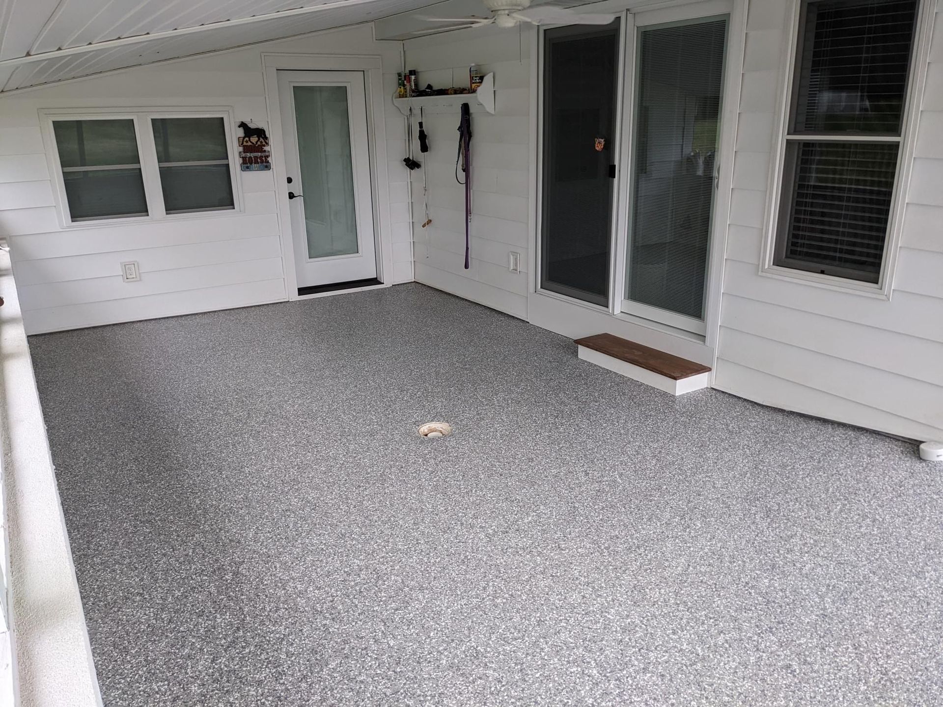 A porch with a gray concrete floor and a white house in the background.