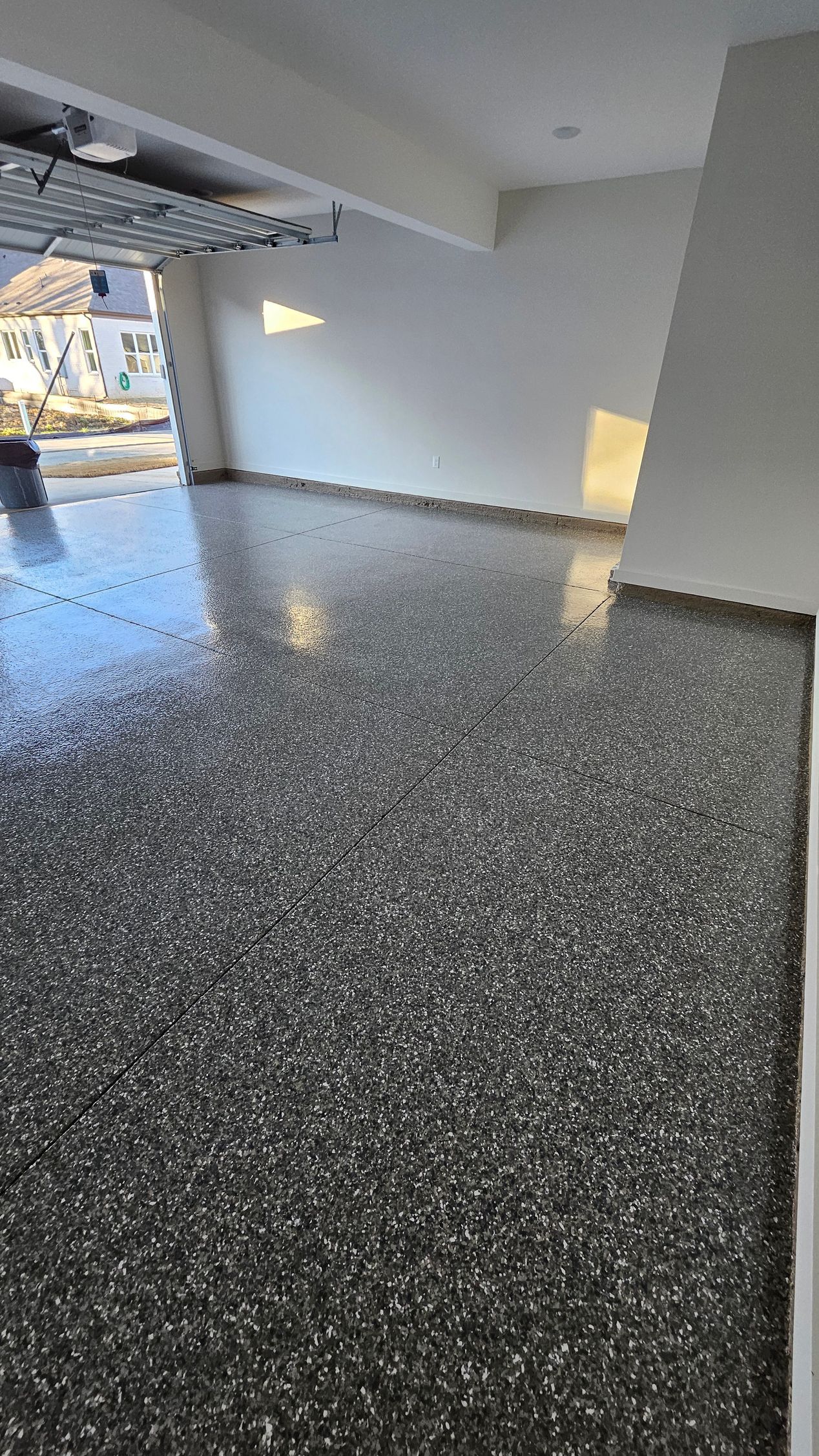 Dark speckled floor, white walls, and bright sunlight shining inside a building.