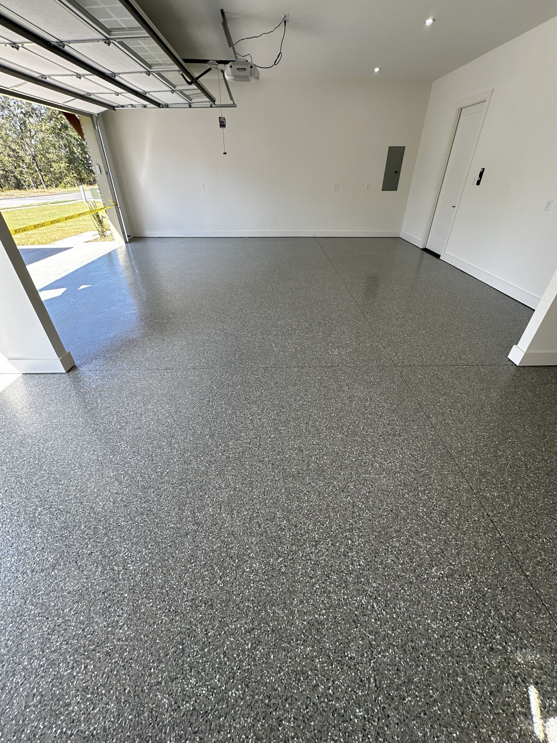 Empty garage with gray speckled epoxy flooring, white walls, and an open garage door.