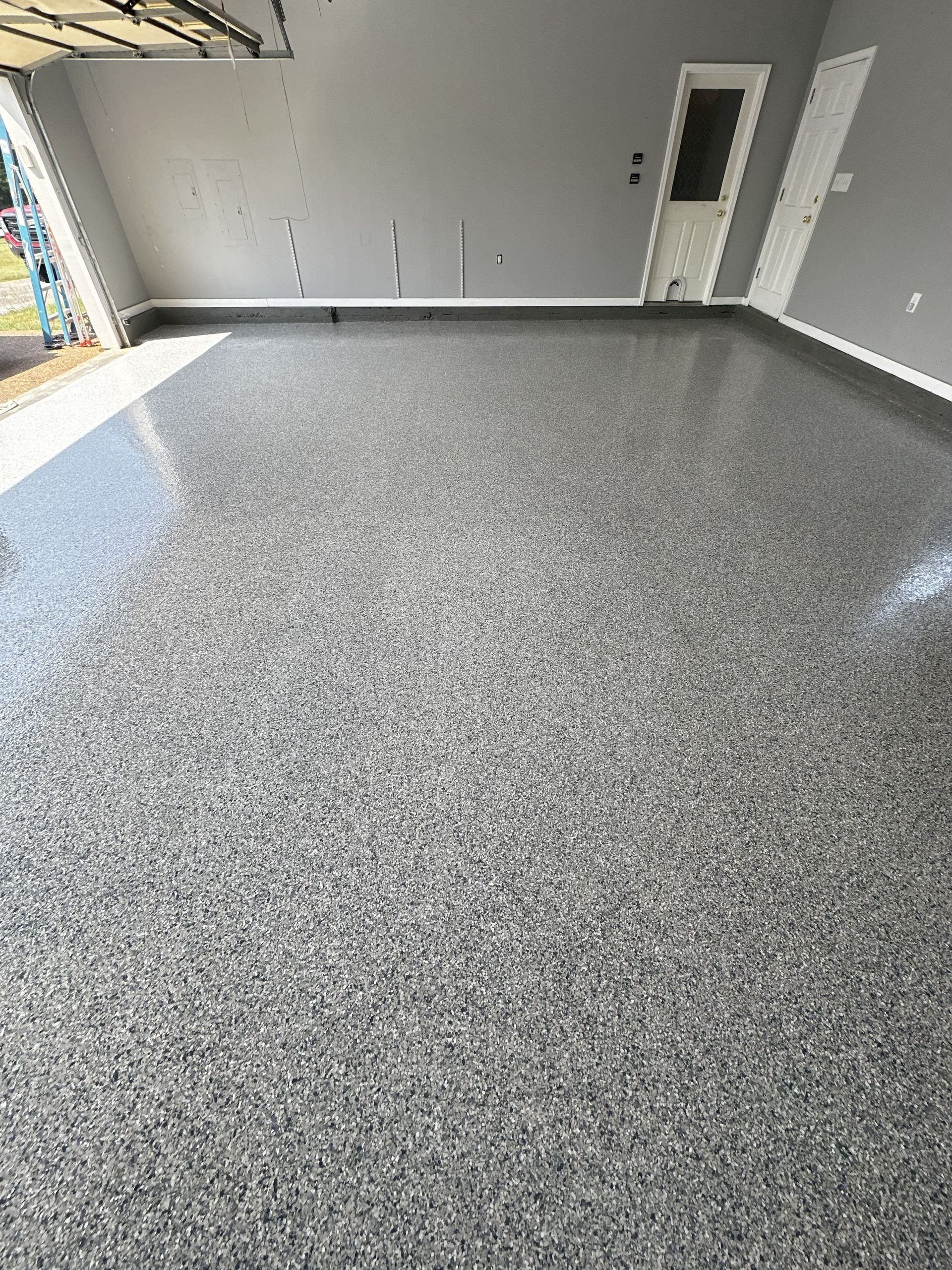 Epoxy-coated garage floor speckled with gray, black, and white chips. Light reflects off the glossy surface.