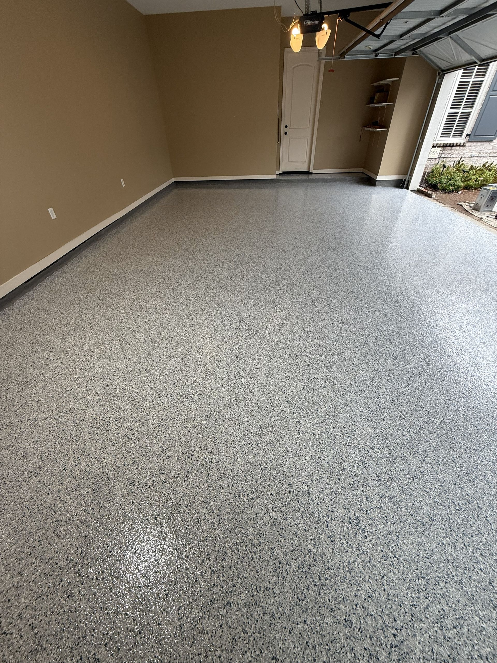 Garage with speckled epoxy floor, beige walls, and open garage door.