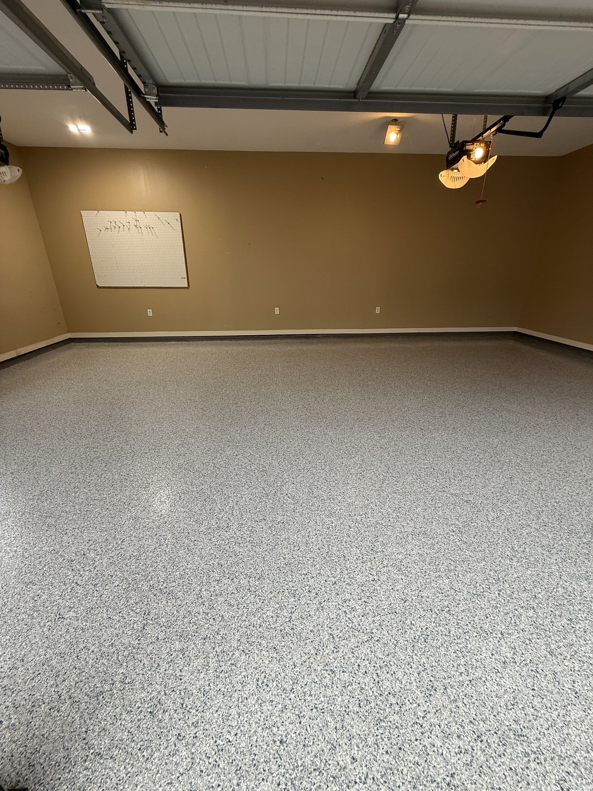 Interior of a garage with a speckled gray epoxy floor and tan walls.