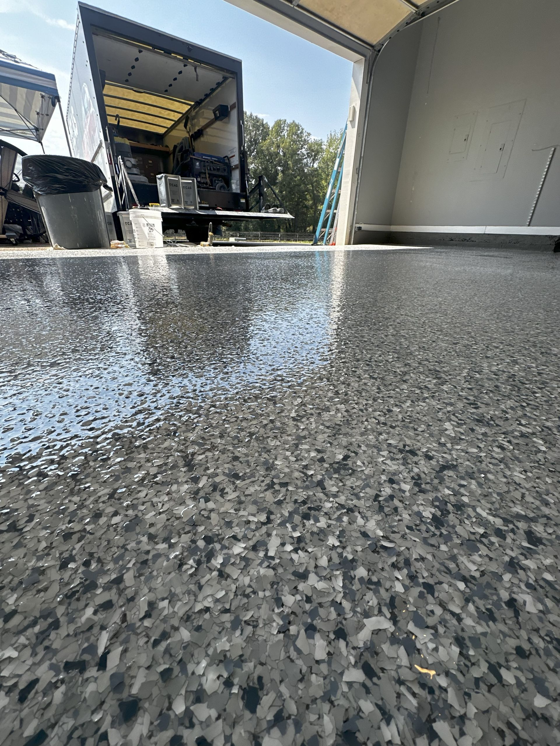Close-up of a speckled, gray epoxy floor in a garage; a truck is visible in the background.