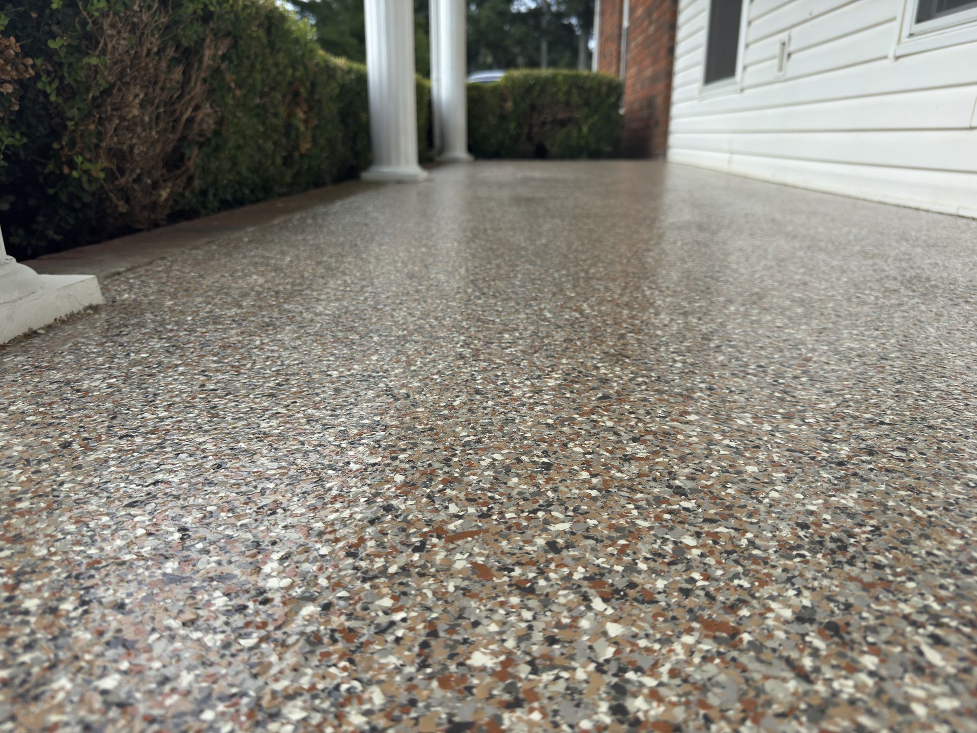 Close-up view of a speckled, glossy concrete porch floor. Brown, gray, and white chips are visible.