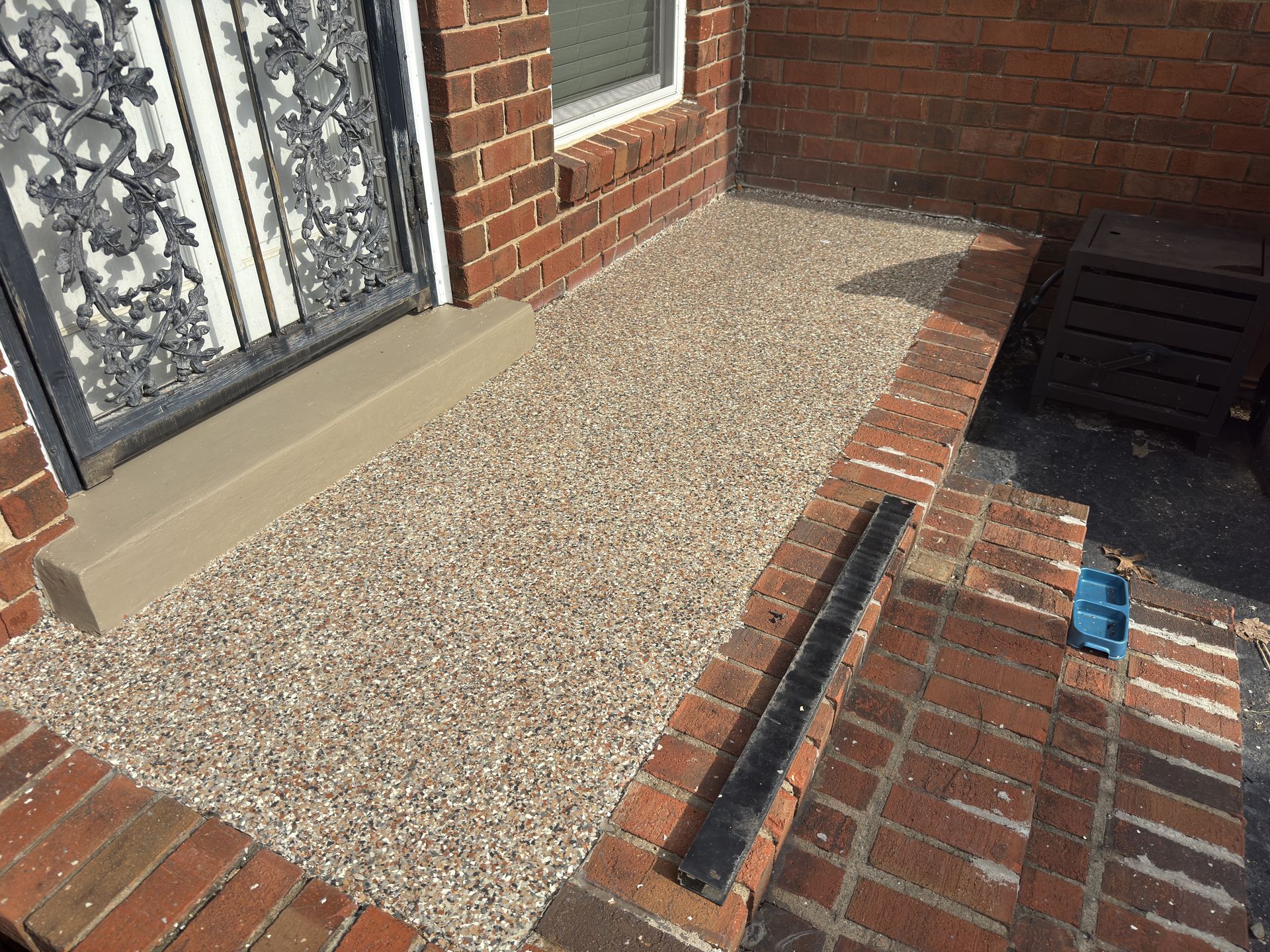 Brick-bordered, gravel-covered entryway to a brick building with a decorative wrought iron door.