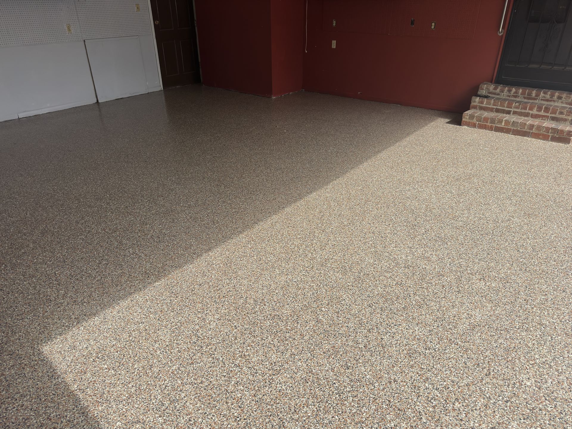 A newly finished speckled epoxy floor in a garage with red walls and brick steps.