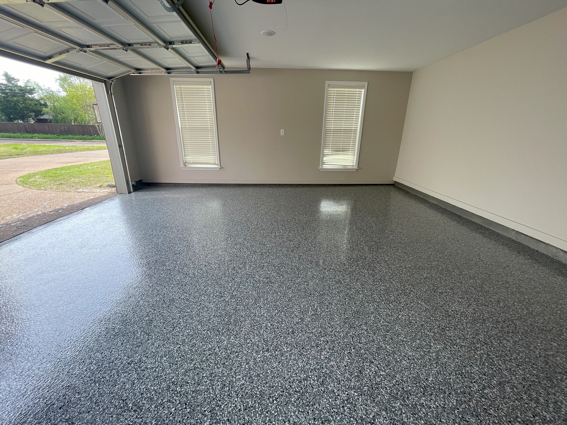 An empty garage with a gray floor and a garage door open.