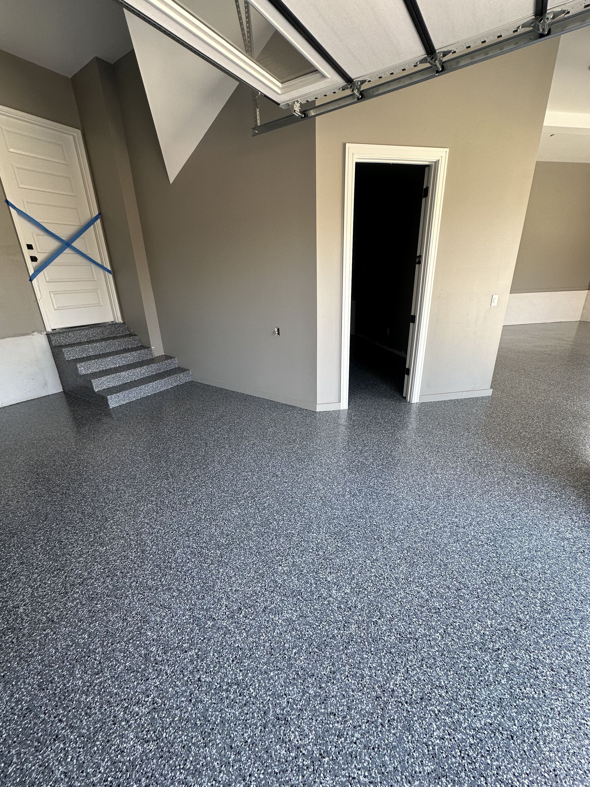 A garage with a gray floor and stairs leading to a door.