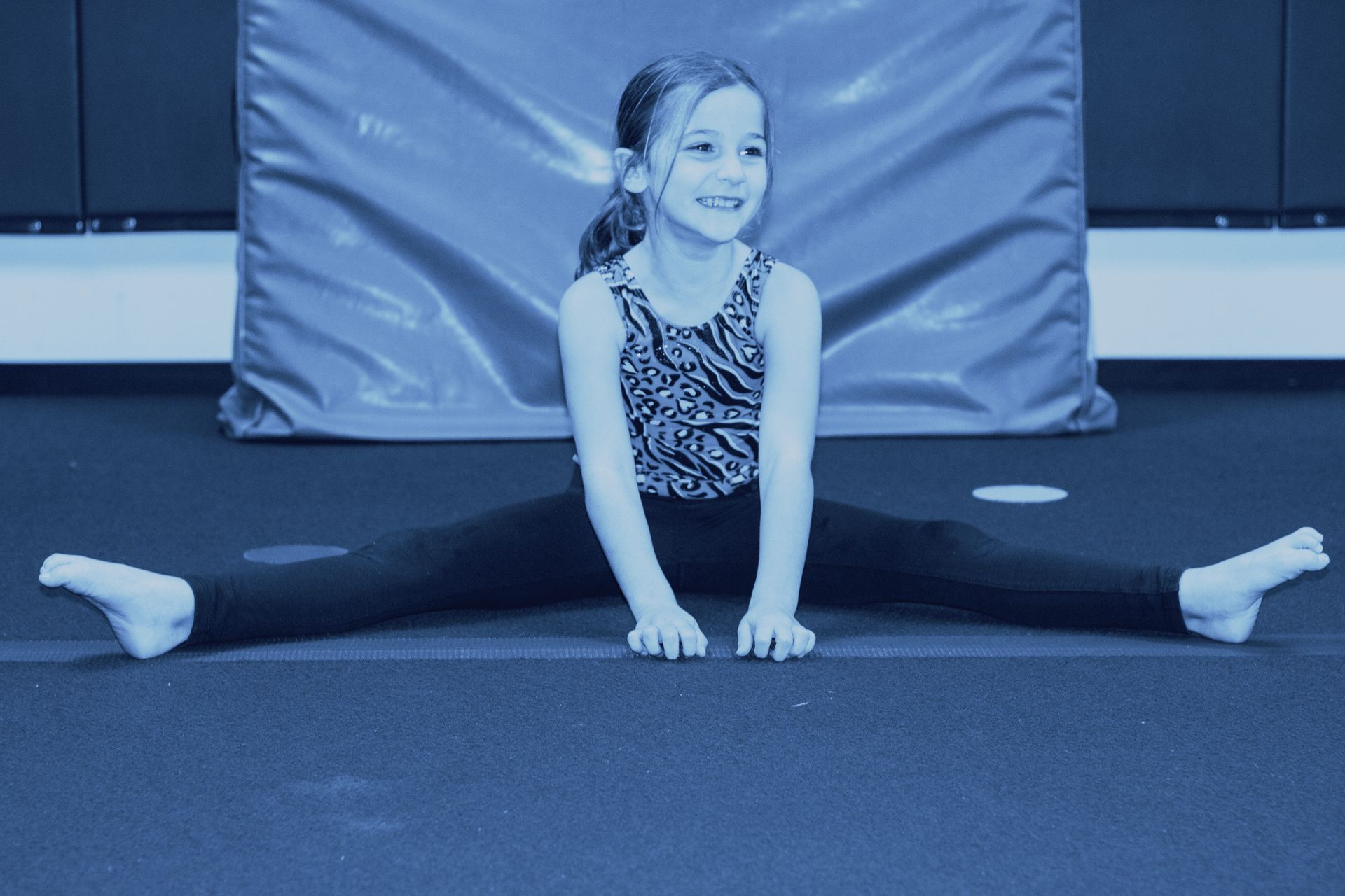 A little girl is doing a split on the floor.