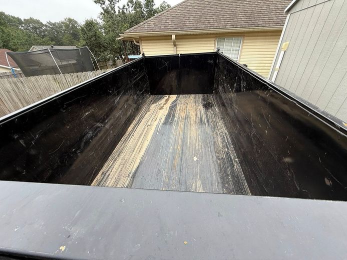 Empty black dumpster viewed from above, with wood siding visible inside.