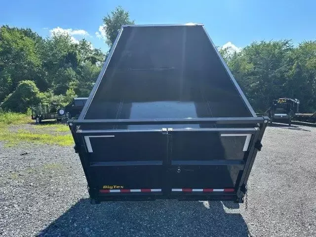 Black dump trailer with open bed, in outdoor setting with trees.