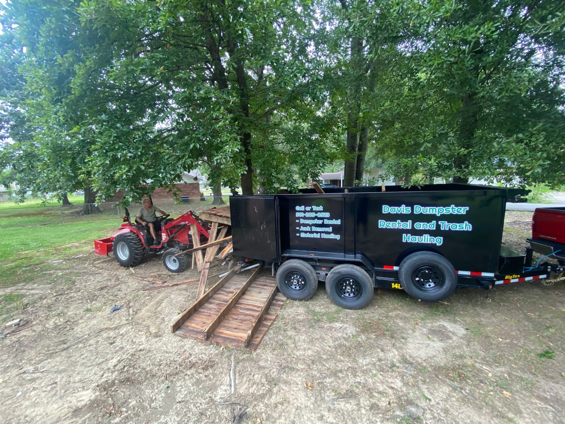 Tractor loading debris into a black dumpster trailer with 