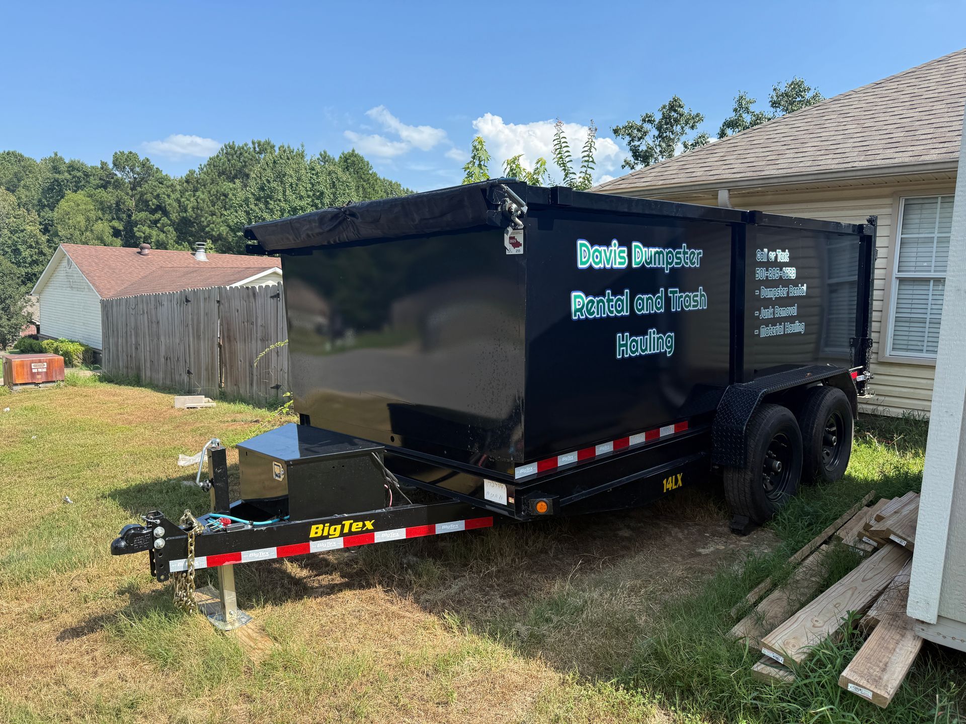 Black dump trailer parked on grass, with rental business name and contact information visible.