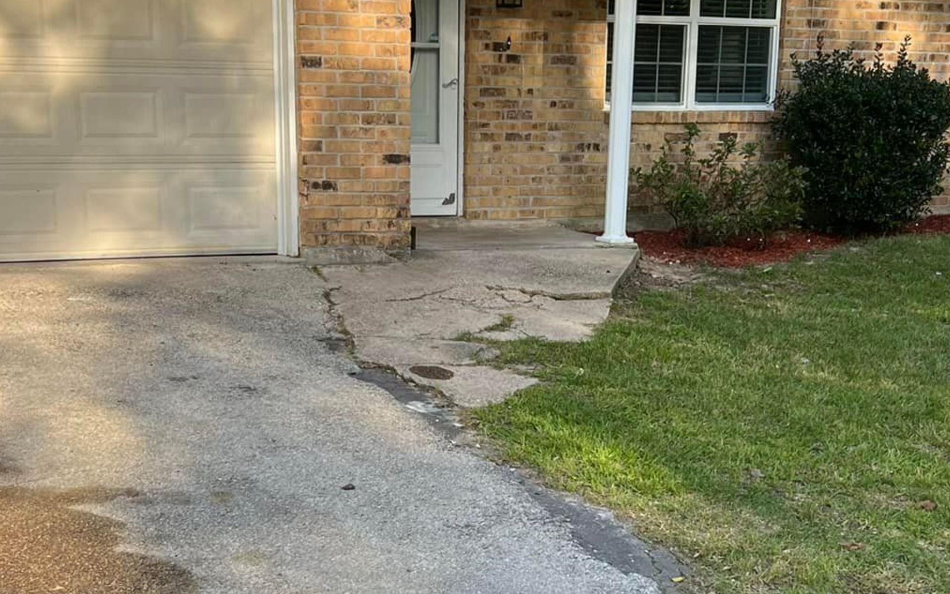 Driveway and brick home with cracked concrete and green grass.