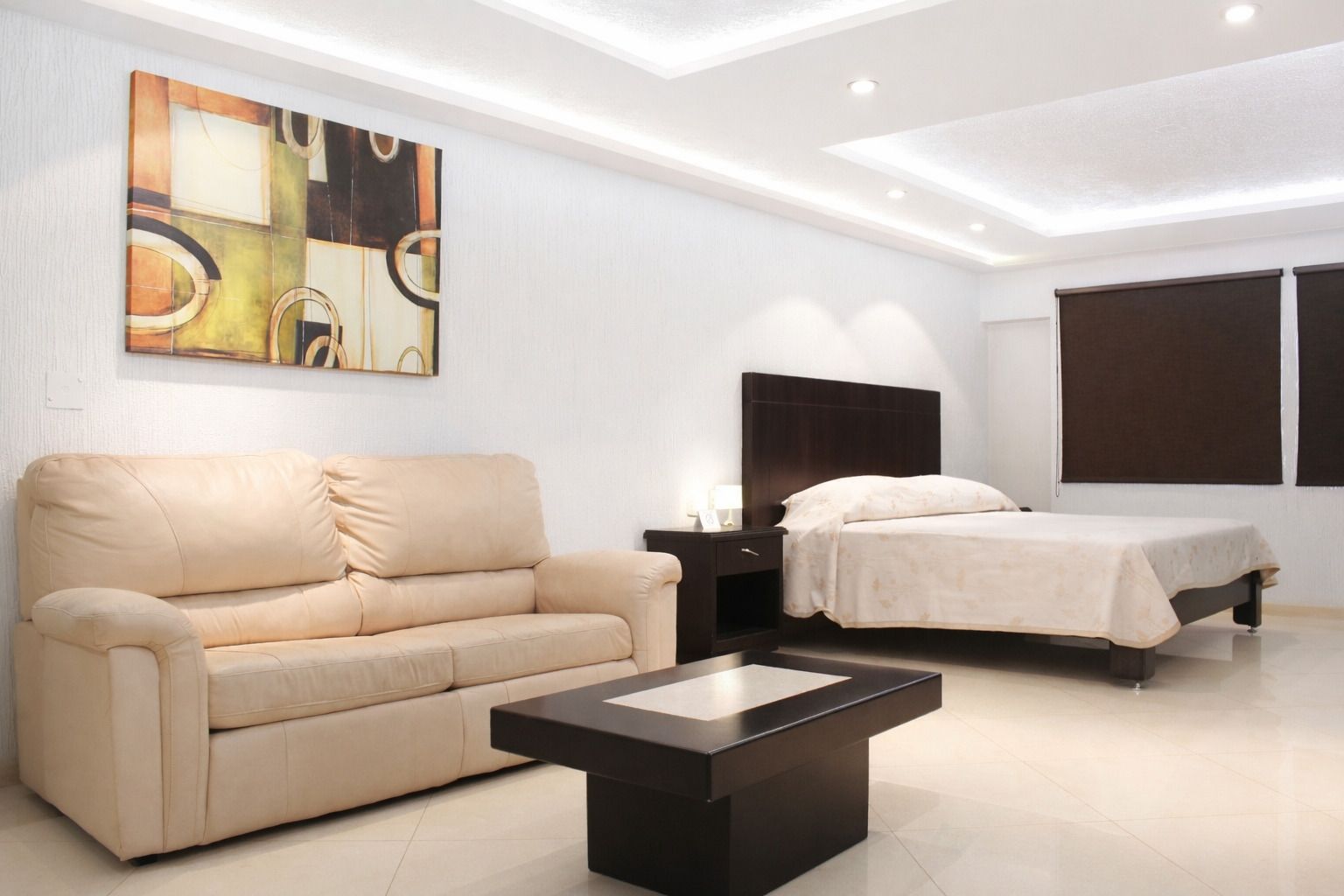 Dos camas en una habitación de hotel, con cabeceros marrones y colchas estampadas. Cortinas marrones y paredes texturizadas.