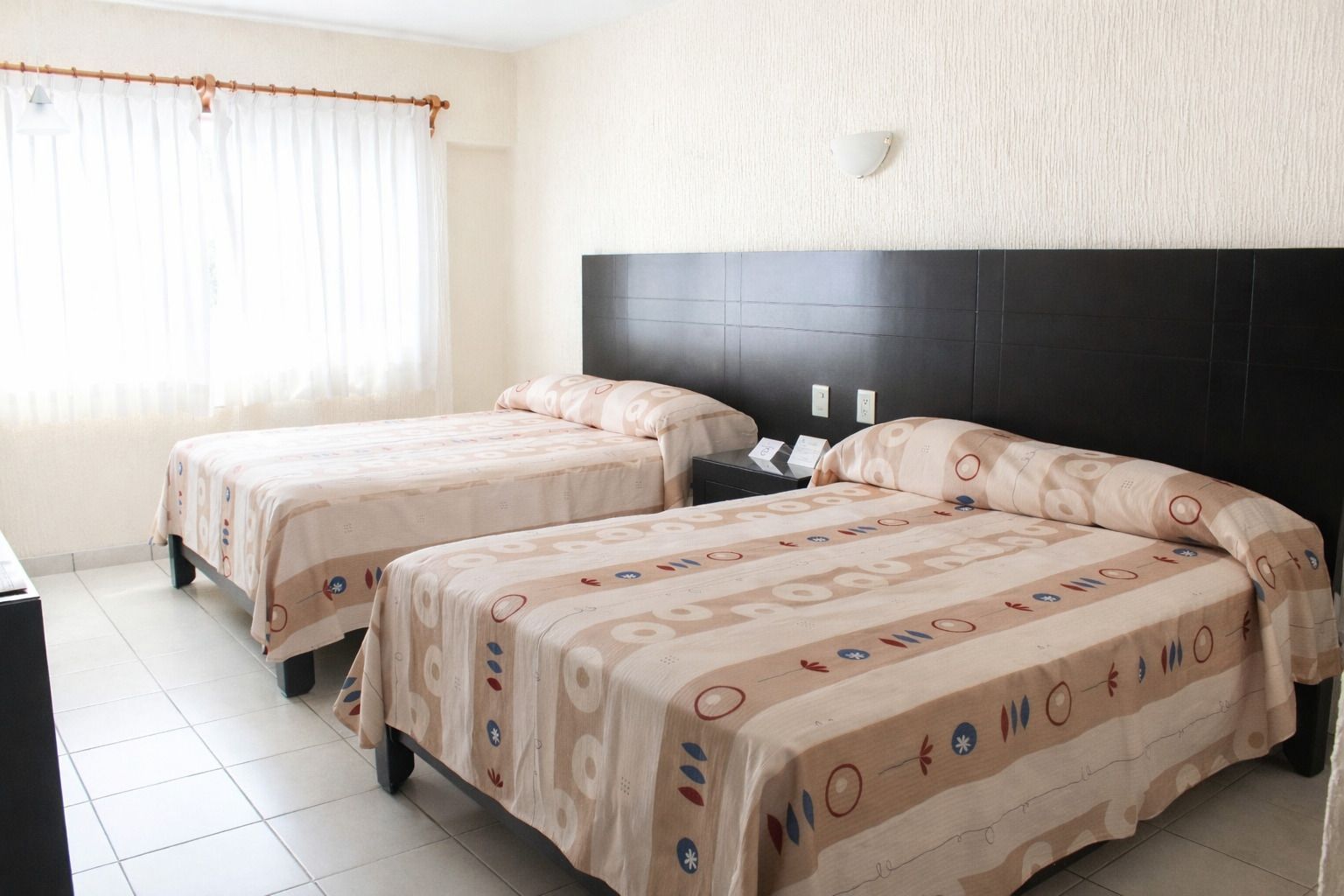 Dos camas individuales en una habitación de hotel con cabeceros marrones y colchas estampadas.