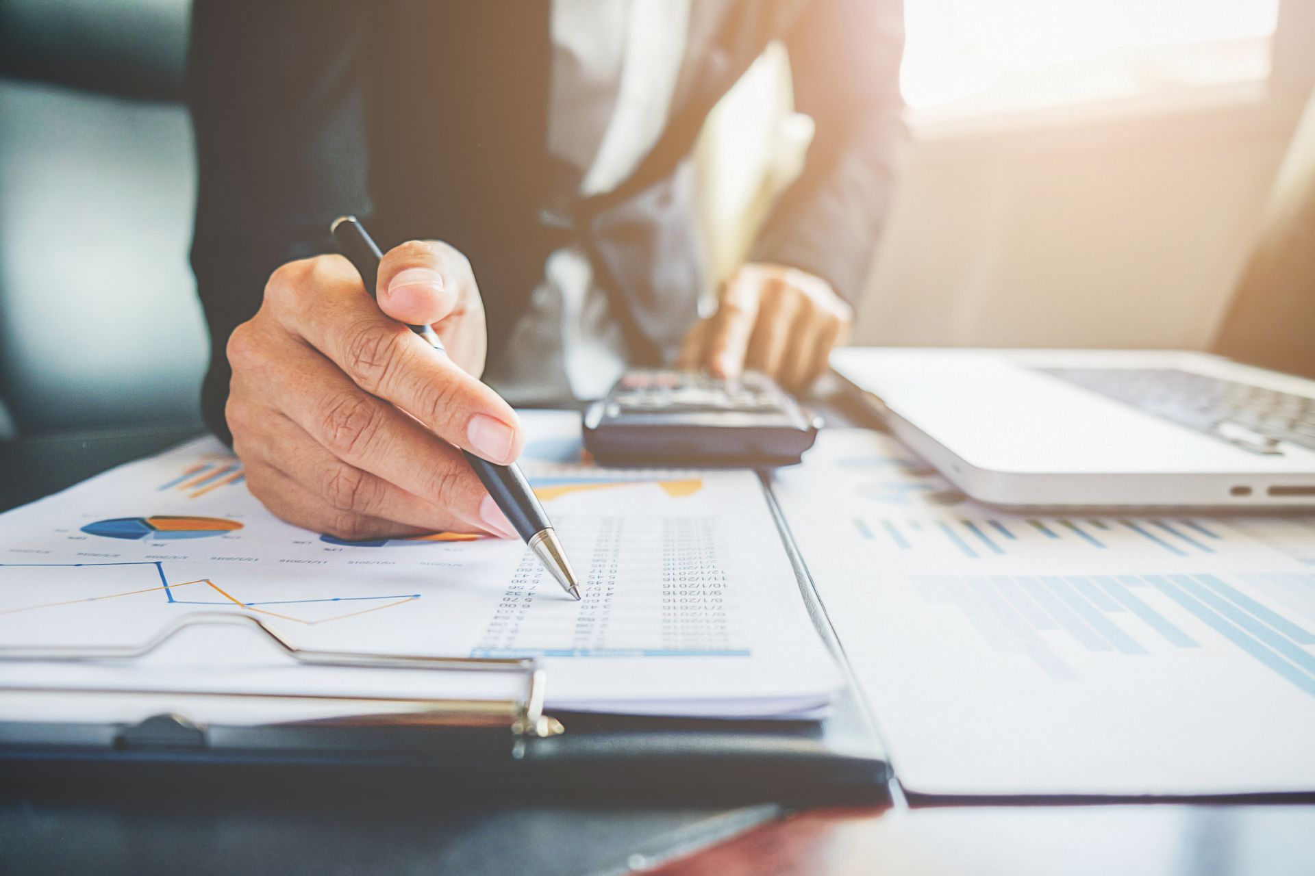 Close-up of a person in business attire using a pen to analyze financial documents