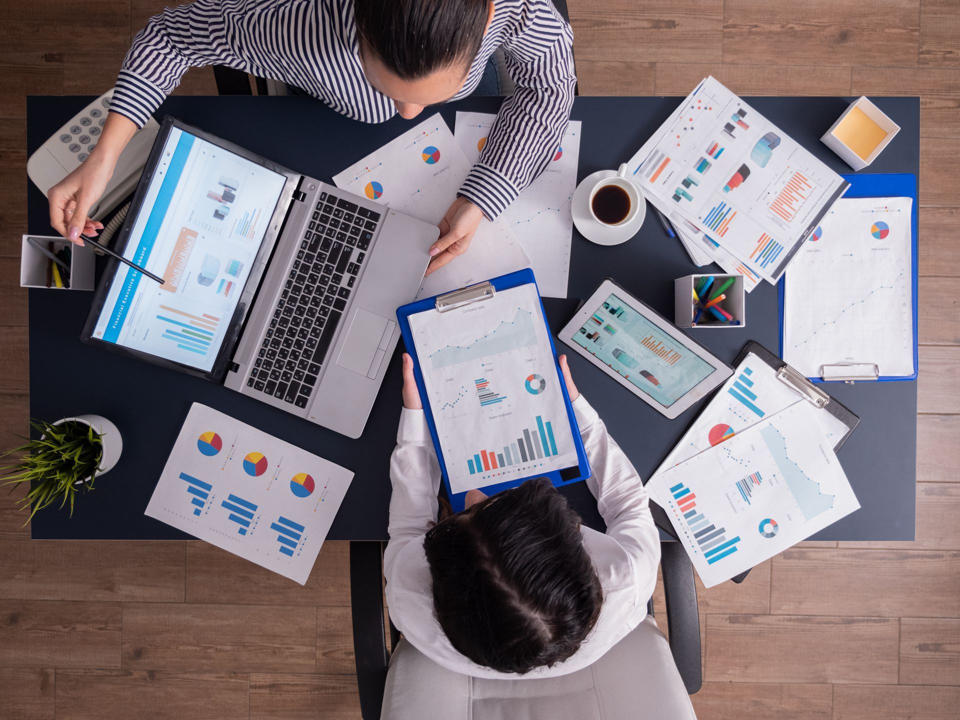Top-down view of two businesspeople working at a desk covered with printed charts