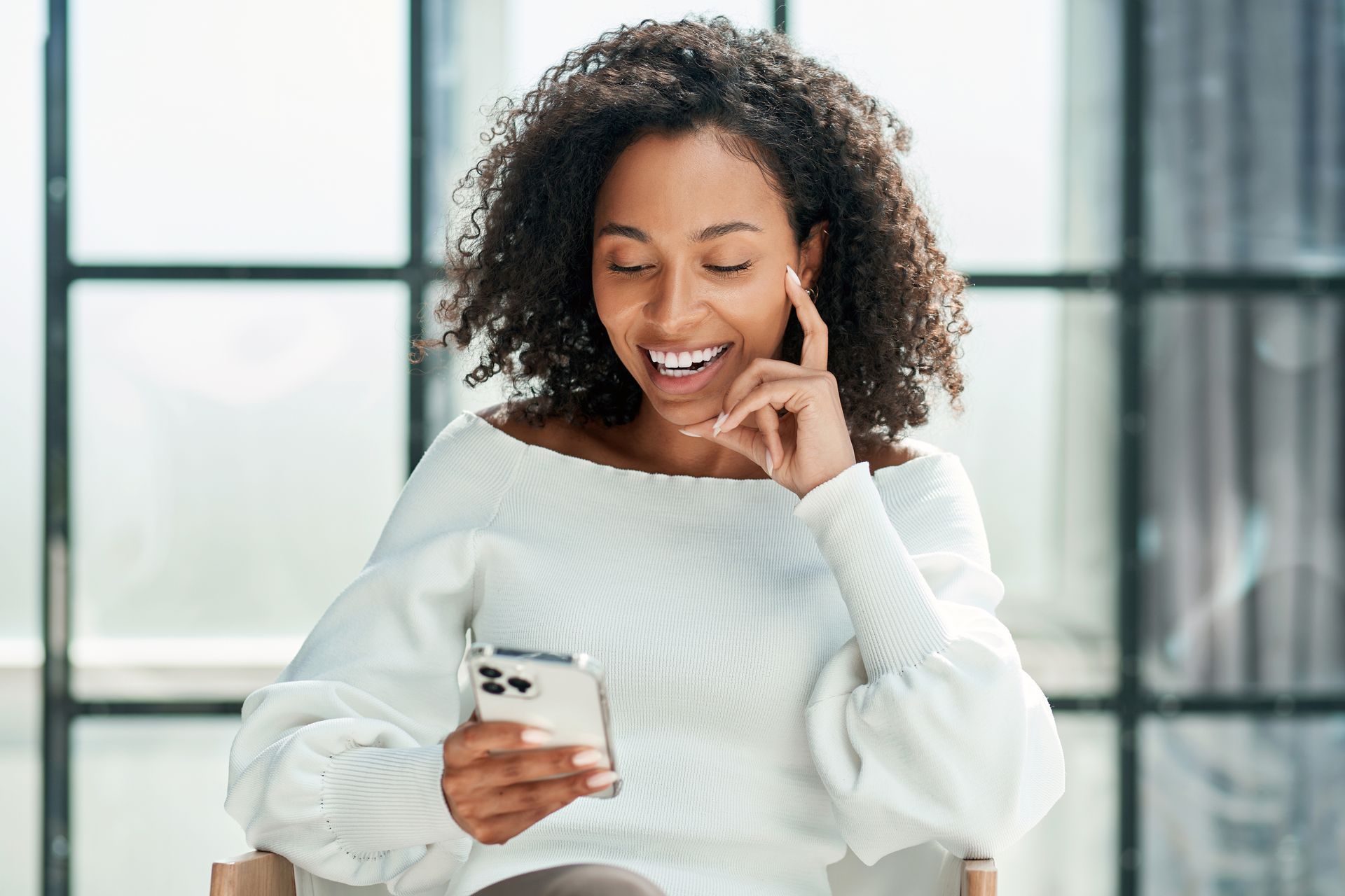 A woman is sitting in a chair looking at her cell phone.