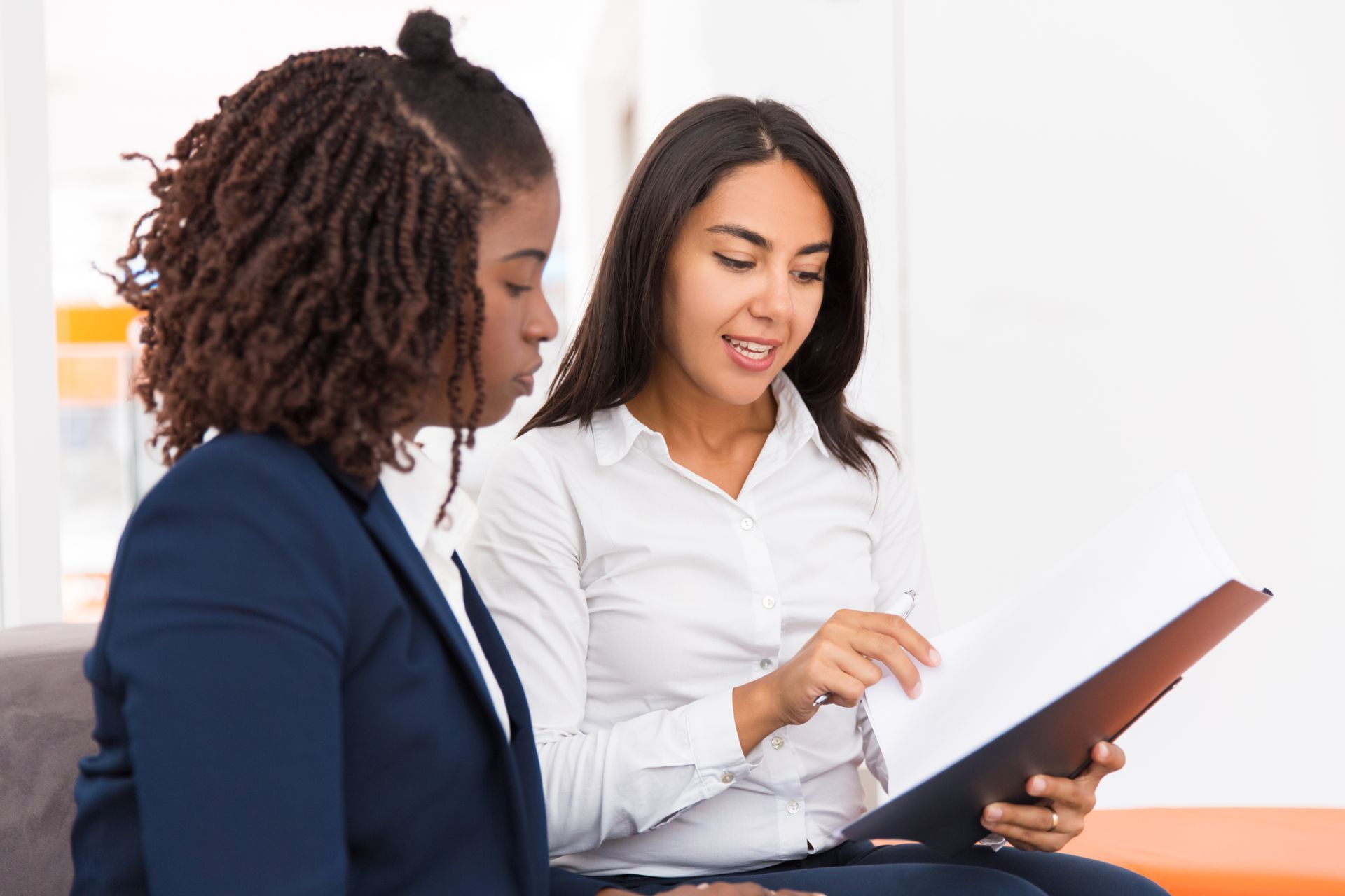 Two women are sitting on a couch looking at a clipboard.