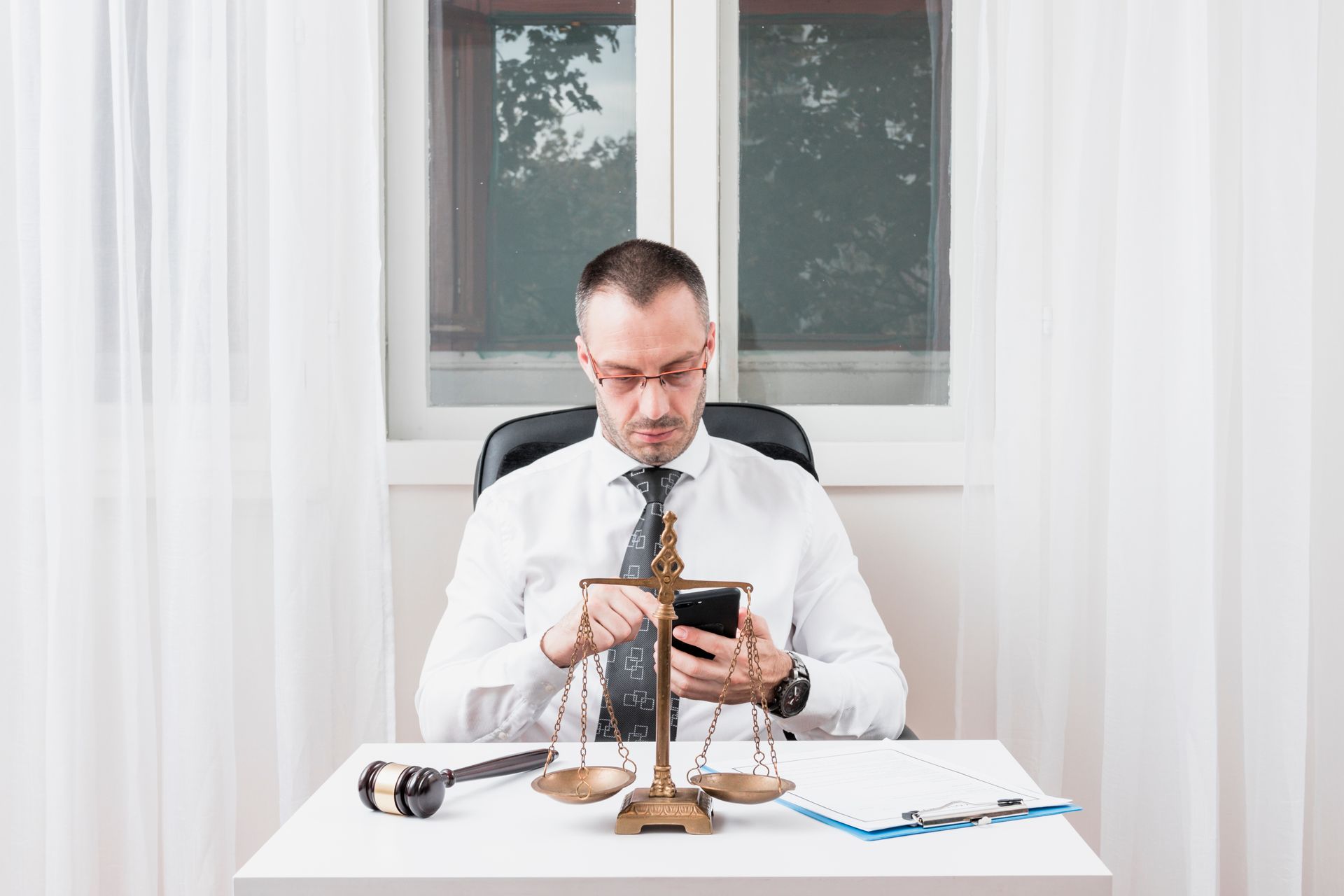 A lawyer is sitting at a desk looking at his cell phone.