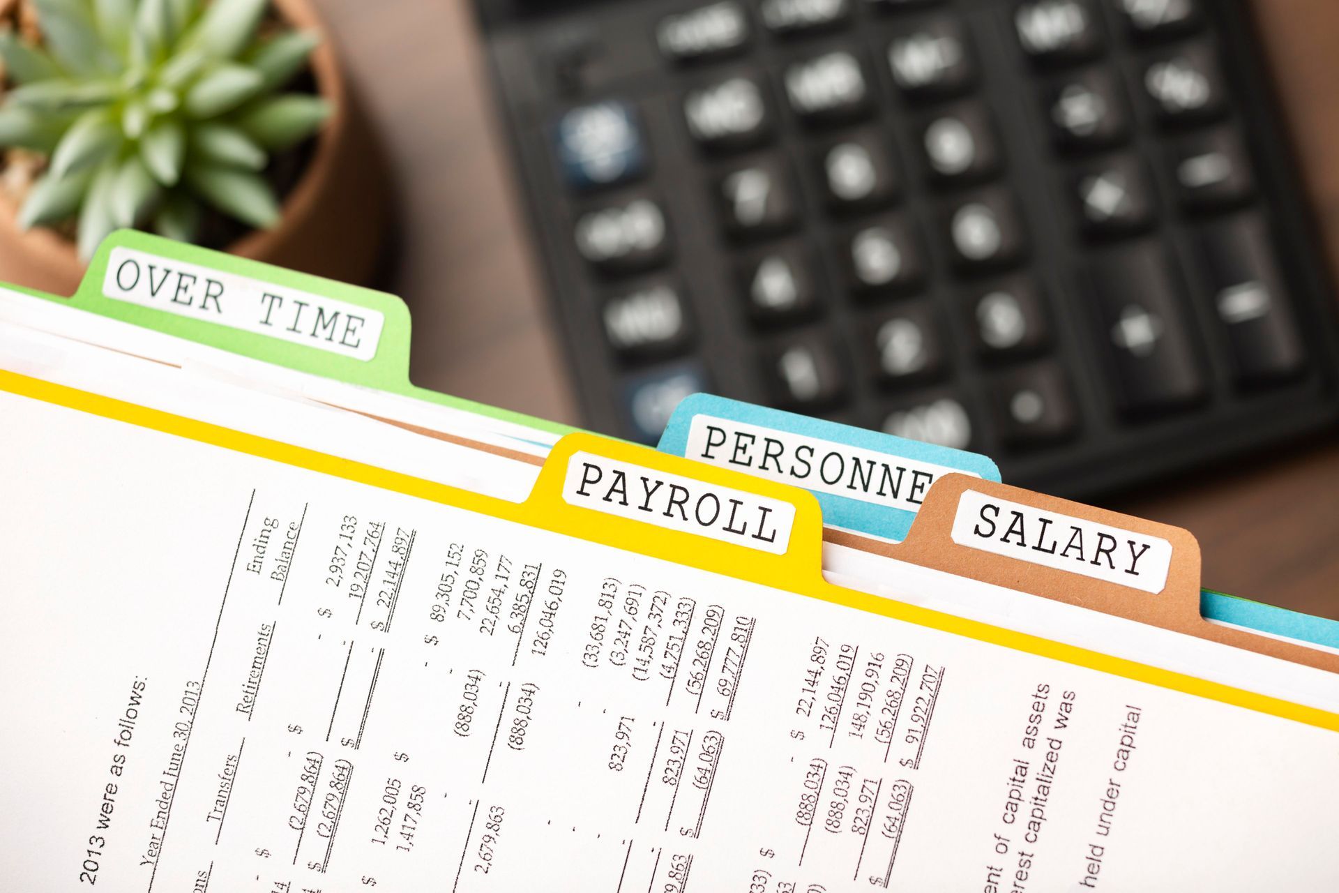 A calculator is sitting on a table next to a binder with tabs for payroll , personnel , and salary.