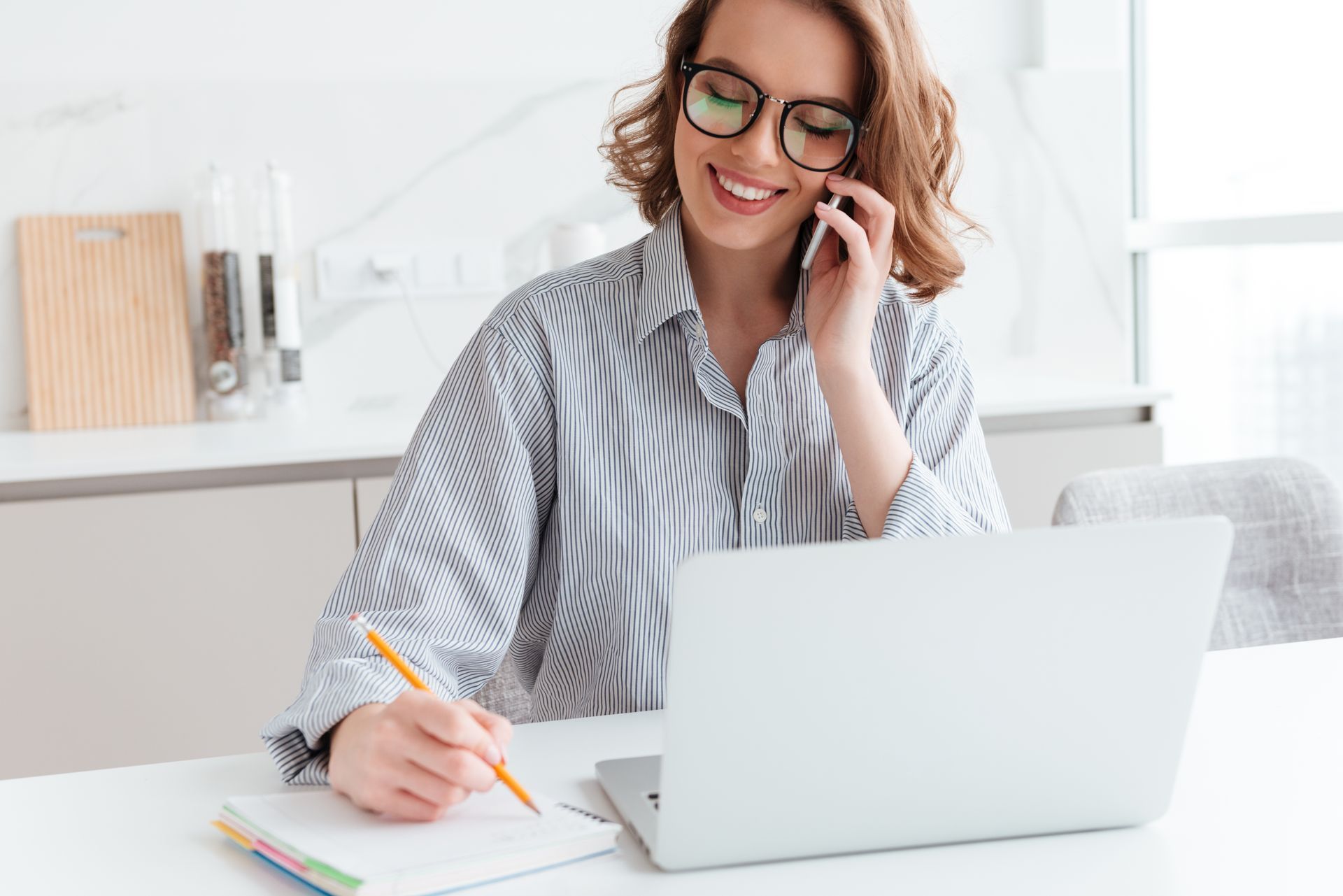 A woman is sitting at a table with a laptop and talking on a cell phone.