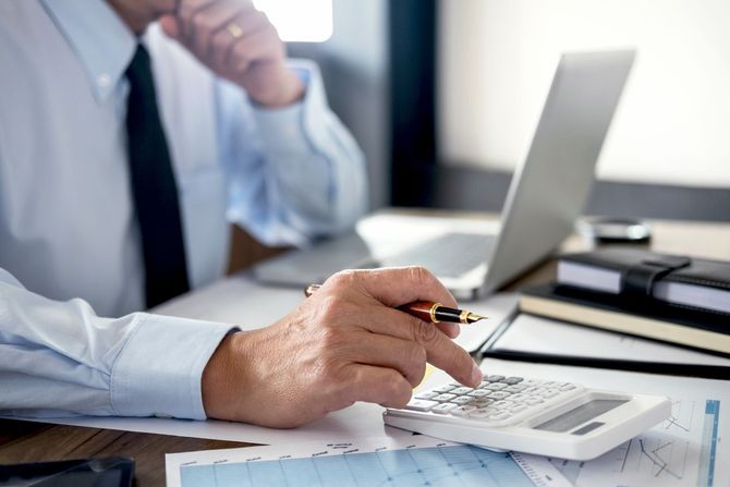 A man is sitting at a desk using a calculator and a pen.
