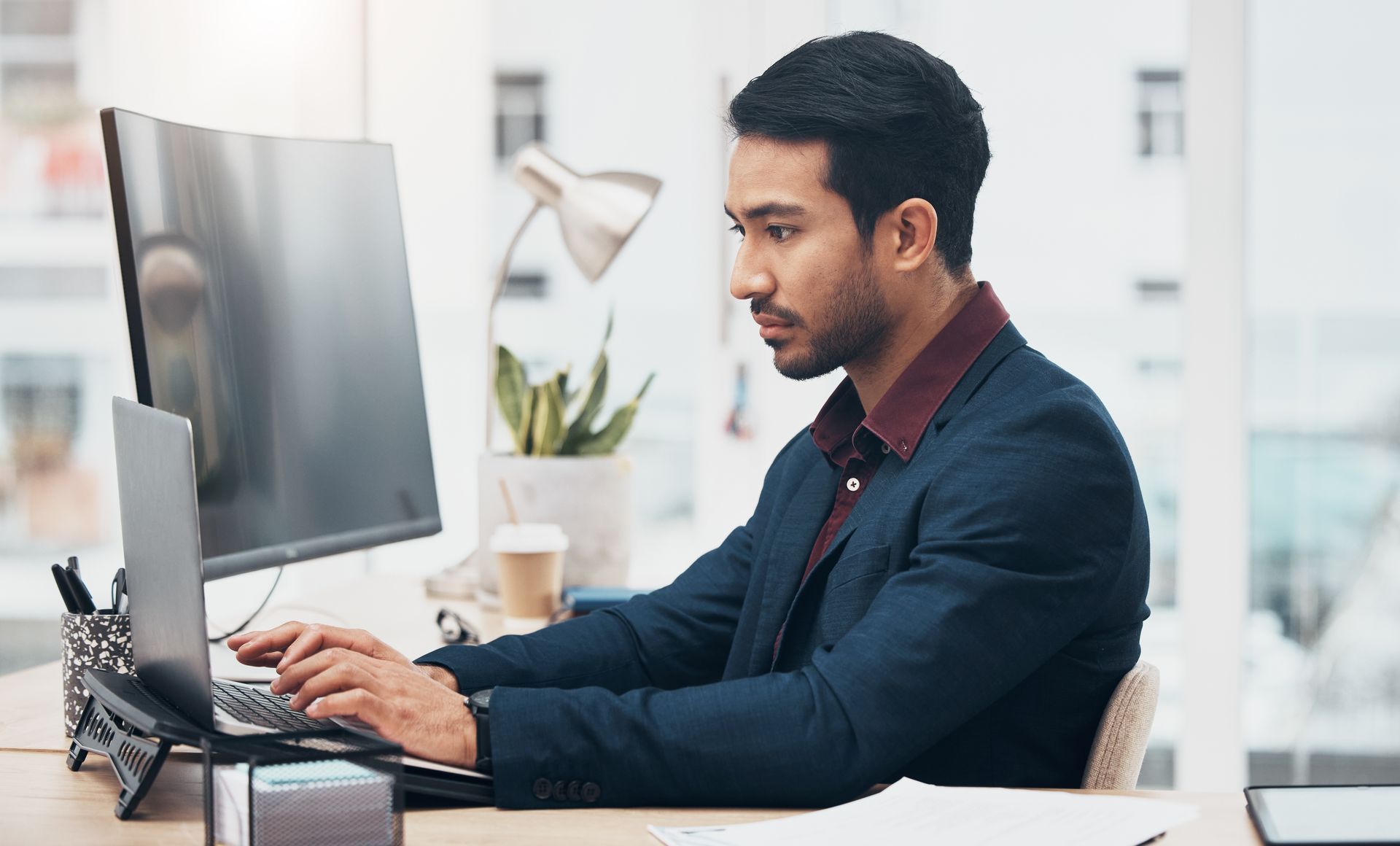 A man is sitting at a desk typing on a laptop computer.