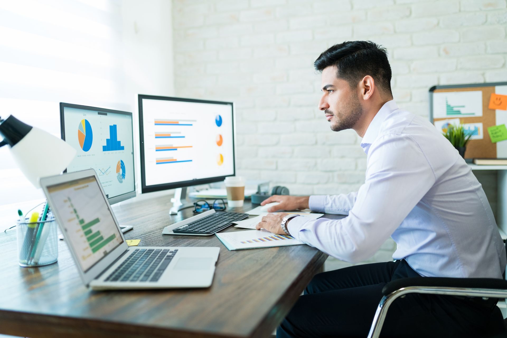 A man is sitting at a desk in front of a computer and a laptop.