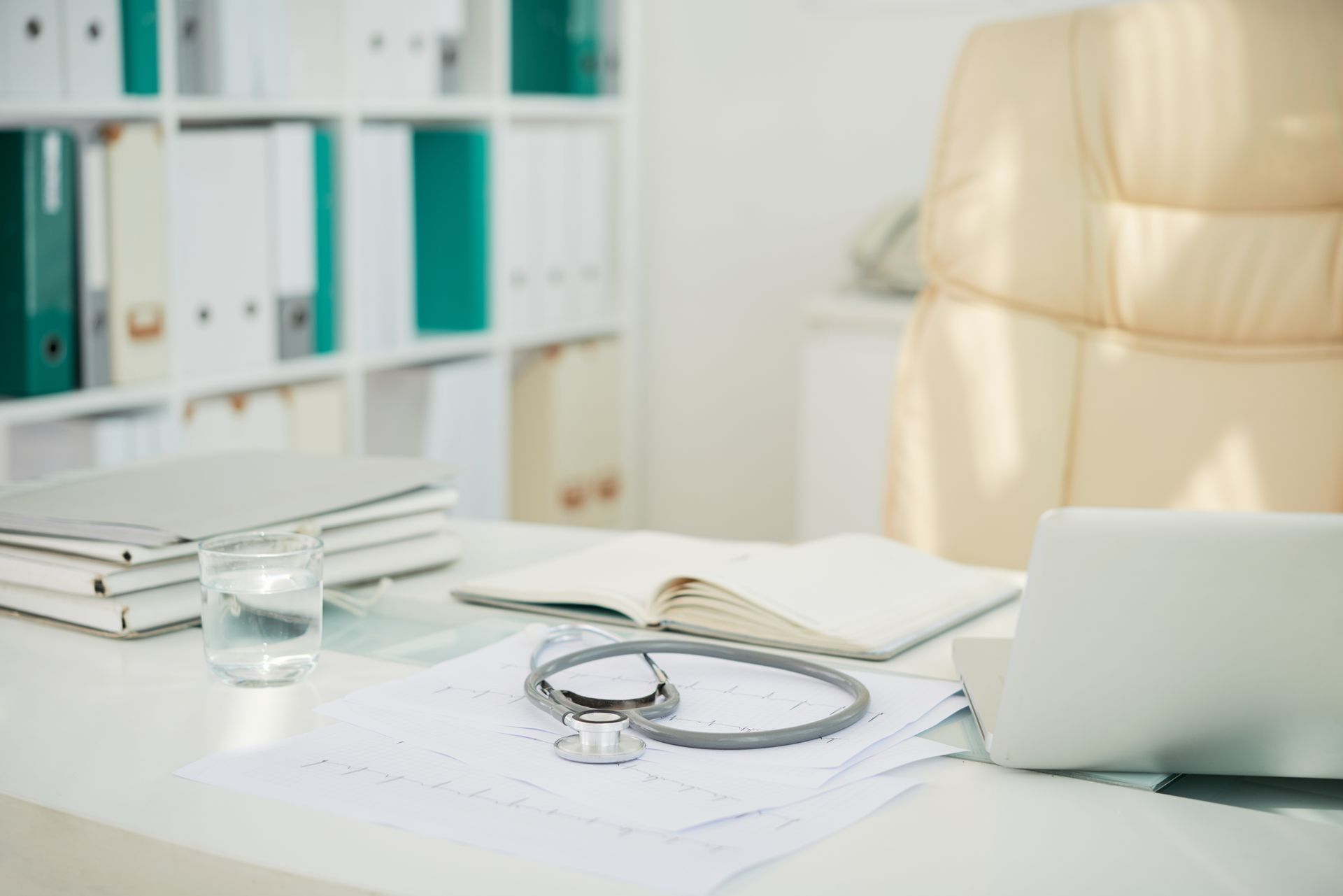A doctor 's desk with a laptop , stethoscope , and a glass of water.