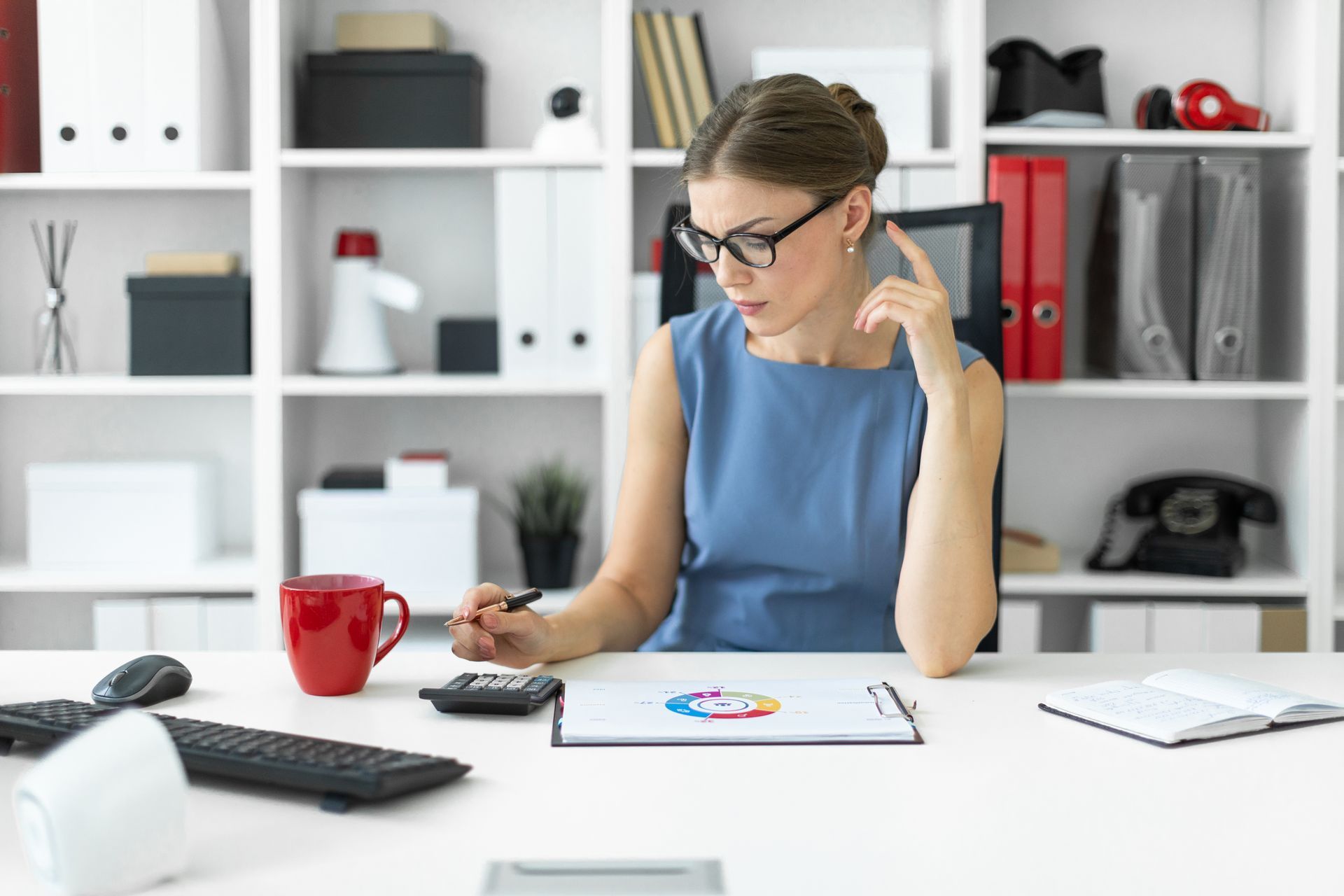 A woman is sitting at a desk in an office using a calculator.