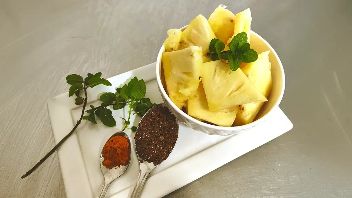 Tigela branca com pedaços de abacaxi, cúrcuma linhaça e um ramo de hortelã