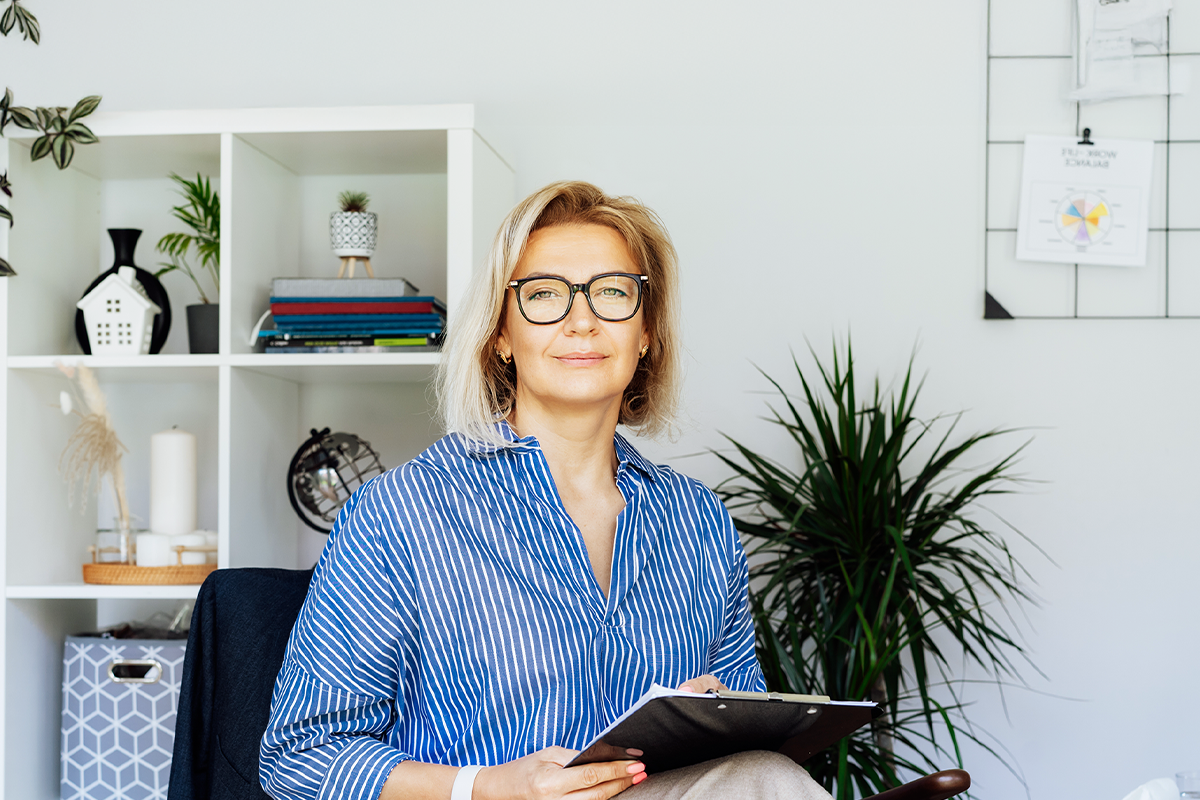 Executiva em camisa listrada azul e óculos, sentada em um escritório