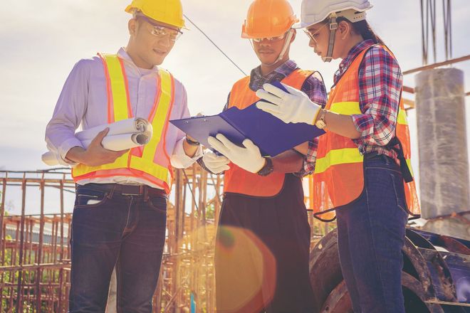 A group of construction workers are looking at a clipboard on a construction site.