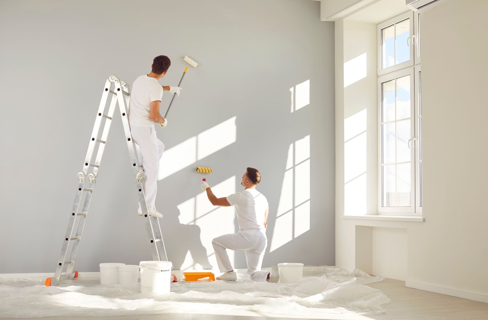 Two men are painting a wall in an empty room.
