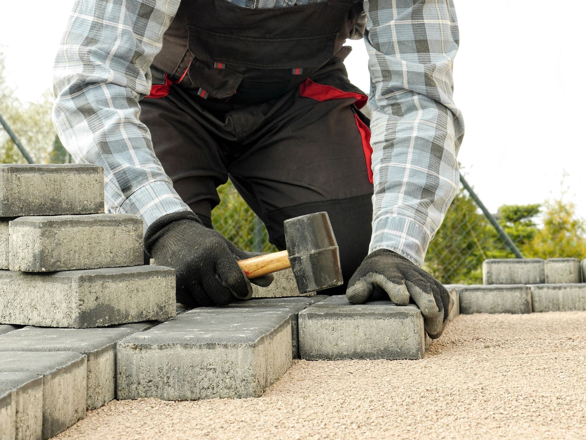 A man is laying bricks on the ground with a hammer.