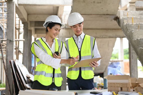 A man and a woman are looking at a clipboard at a construction site.