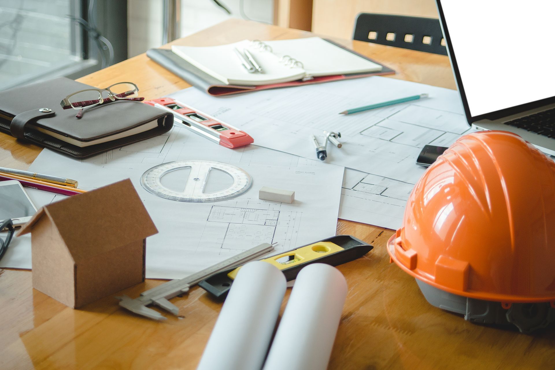 A hard hat is sitting on a wooden table next to a laptop.