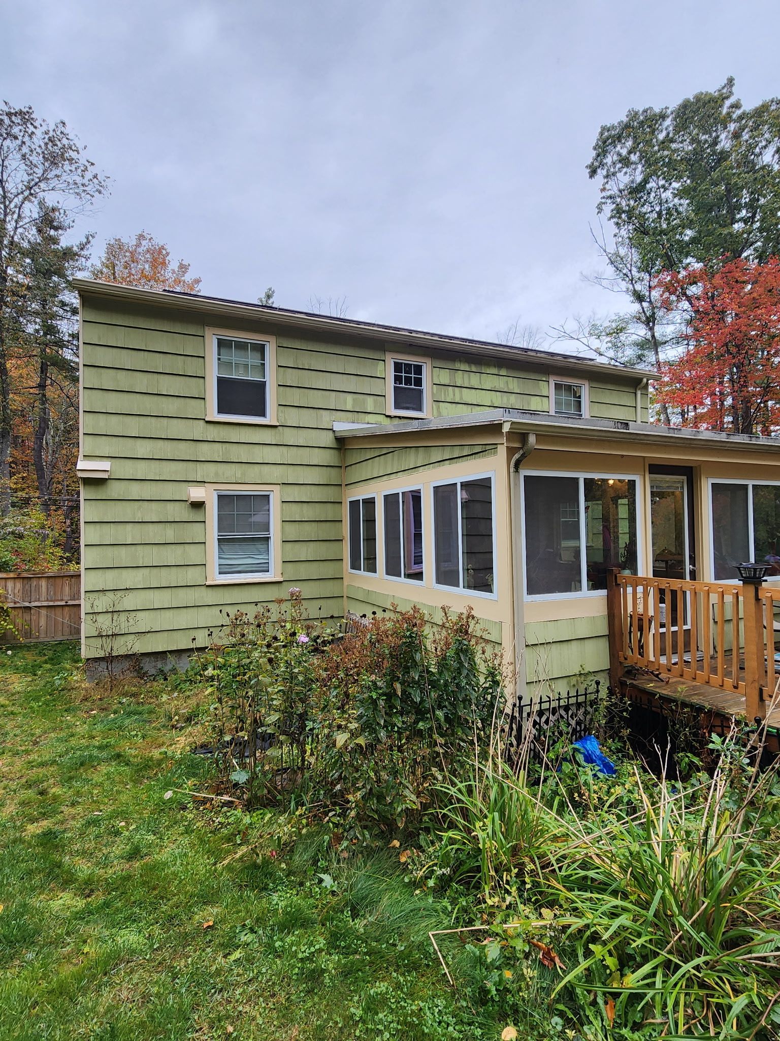 A green house with a screened in porch and a wooden deck.