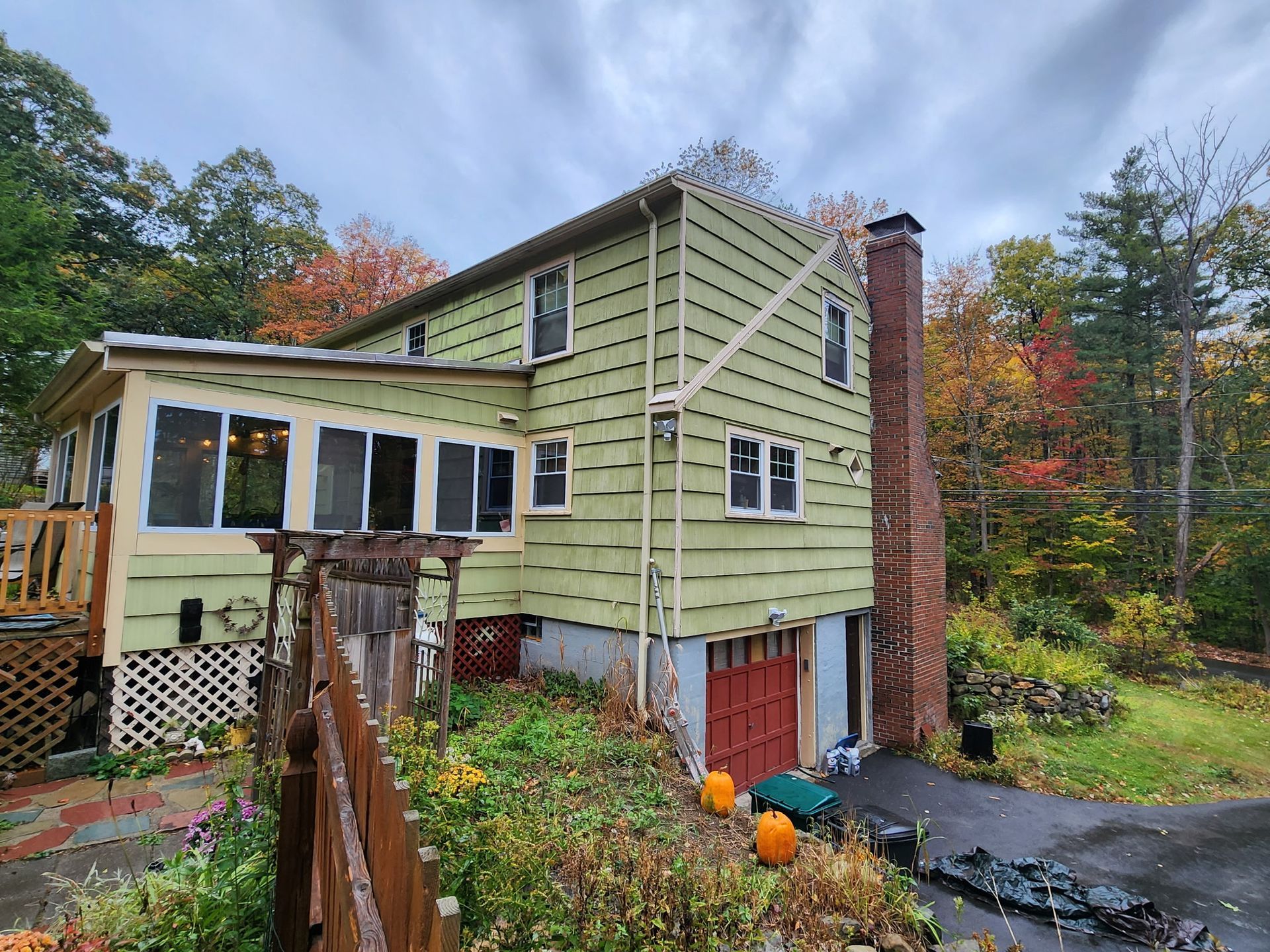 A green house with a red garage door is surrounded by trees.