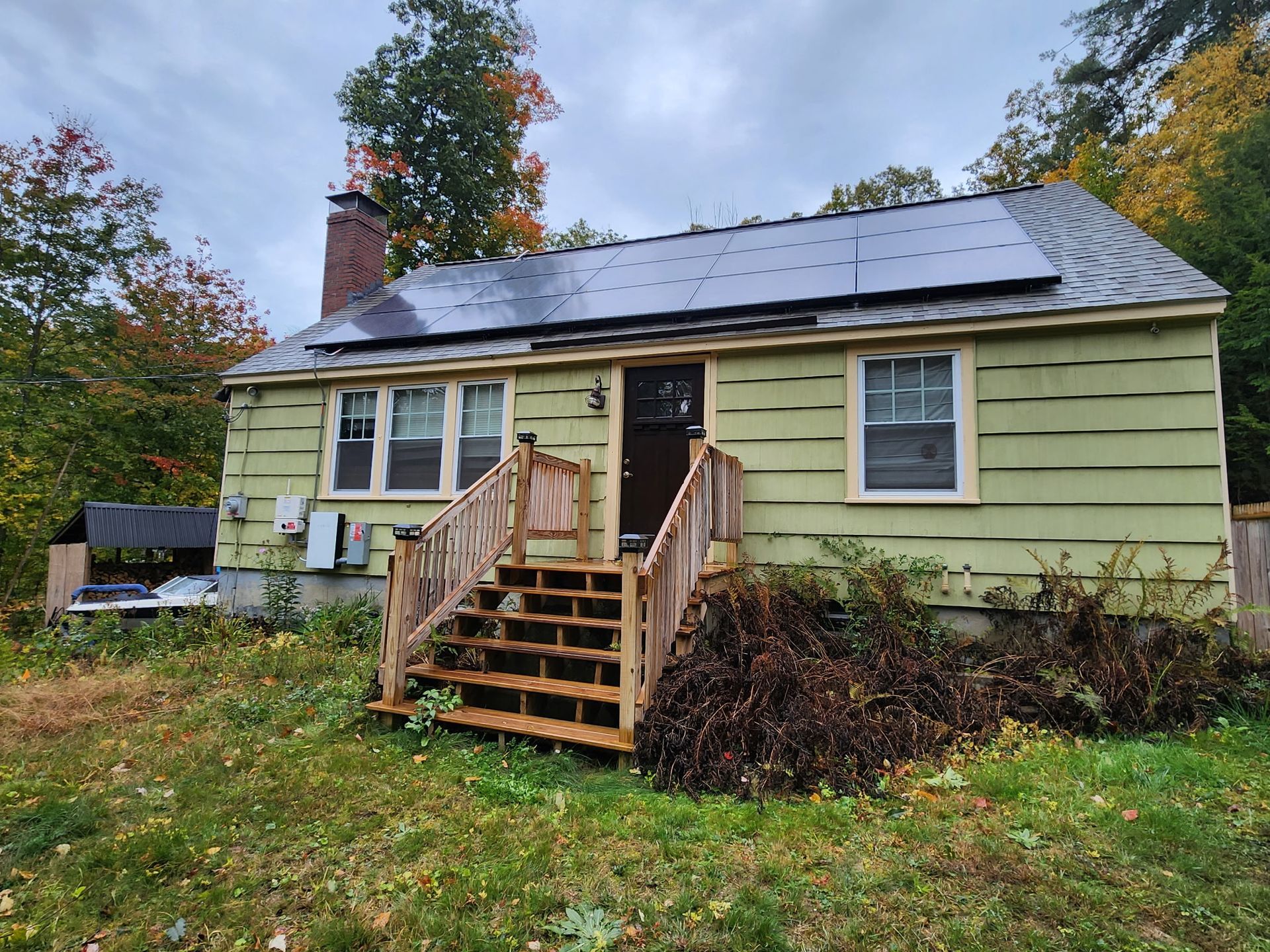 A small green house with stairs and solar panels on the roof.
