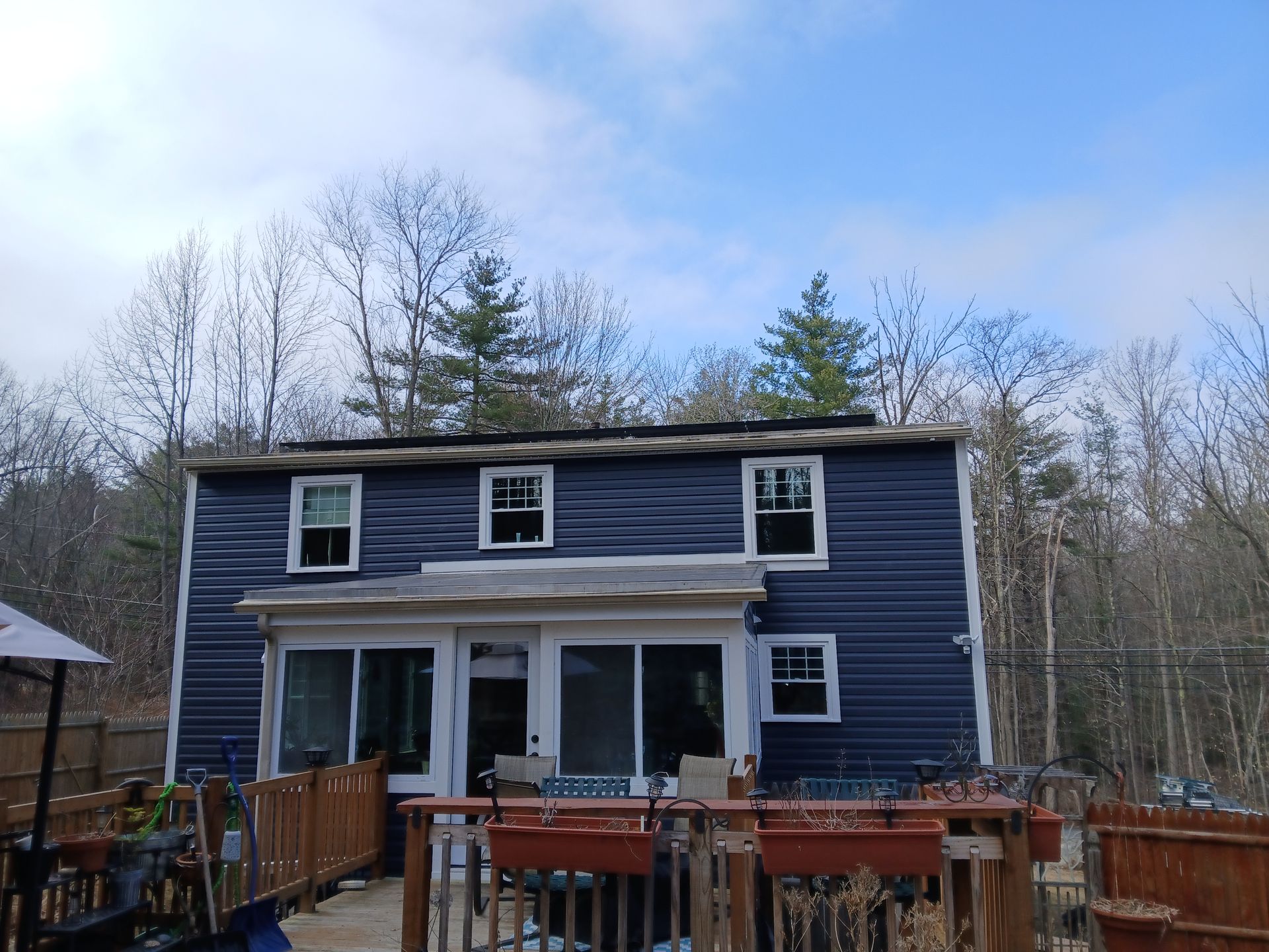 A blue house with a deck in front of it in the woods.
