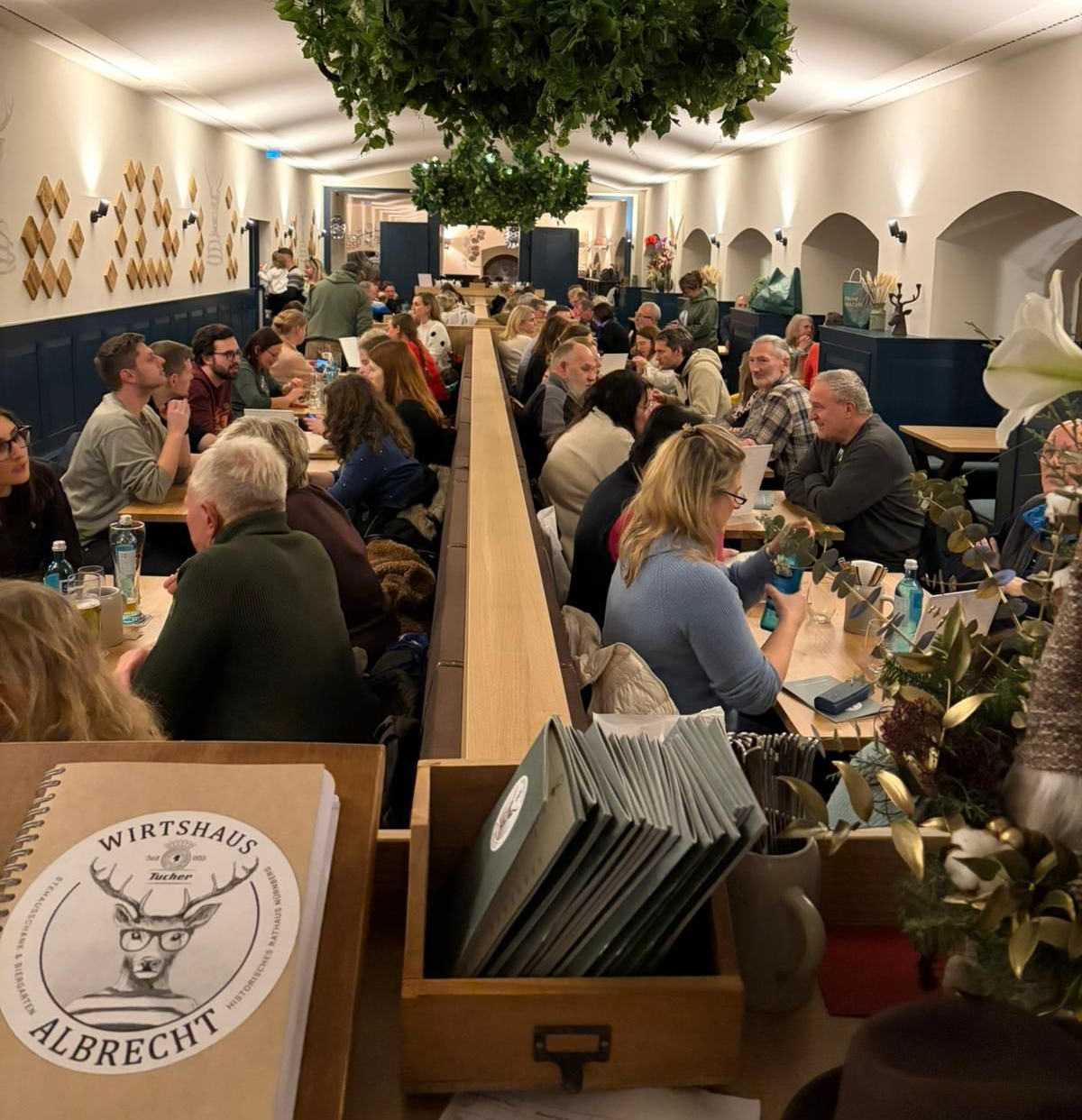 Eine große Stube voller Menschen mit Kronleuchter in der Mitte mit Efeu bekleidet