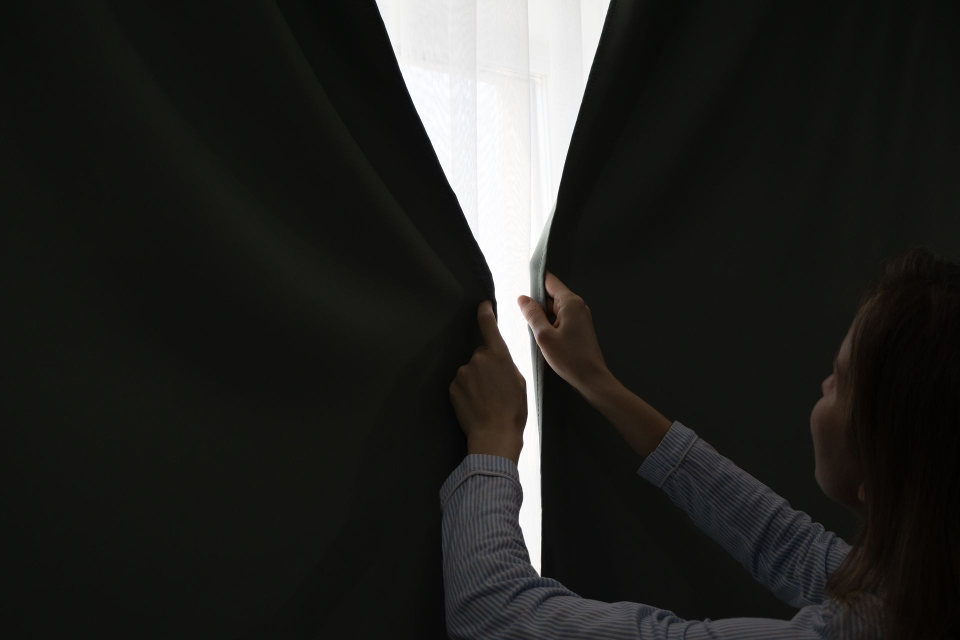 A person closing their apartment curtains to reduce heat from sun rays